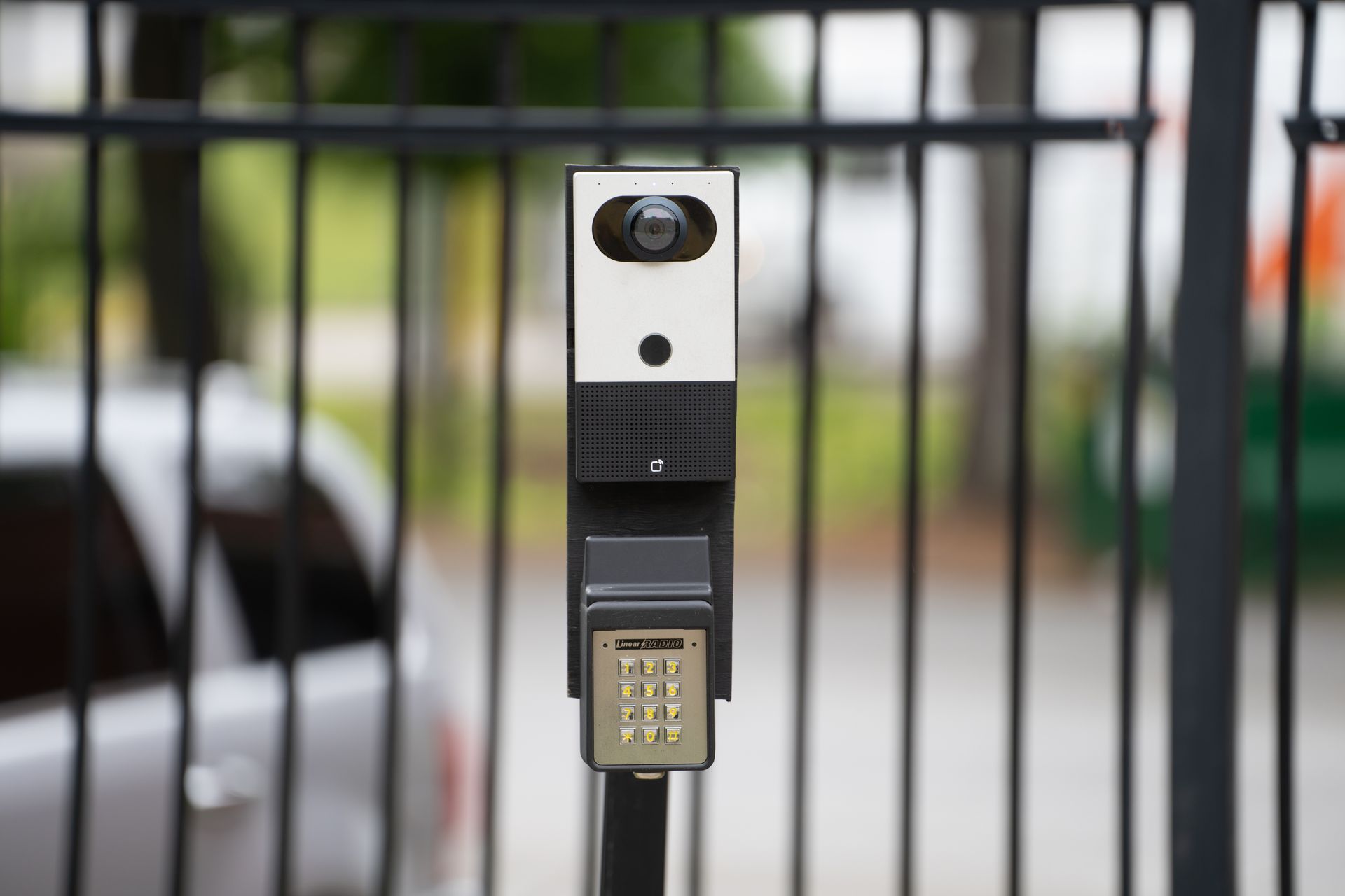 A parking meter with a camera attached to it is sitting next to a fence.