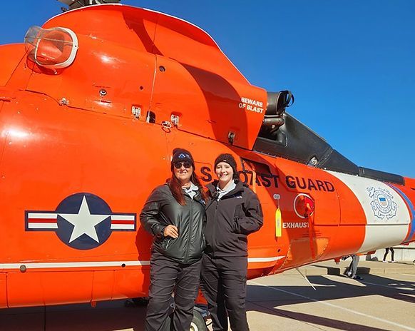 Two women are standing in front of a us coast guard helicopter.