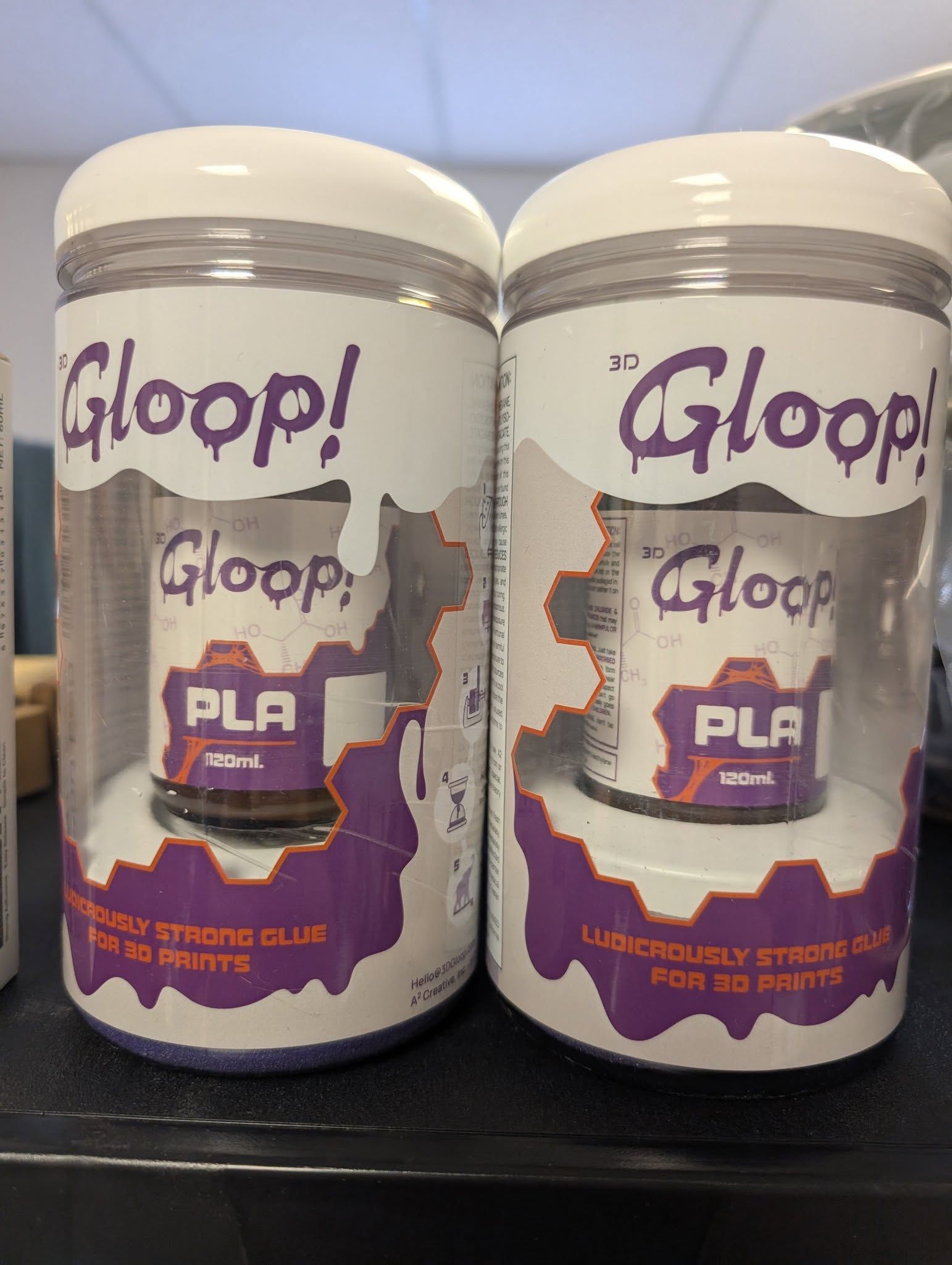 Two white Gloop! PLA filament bottles with purple labels on a black surface.