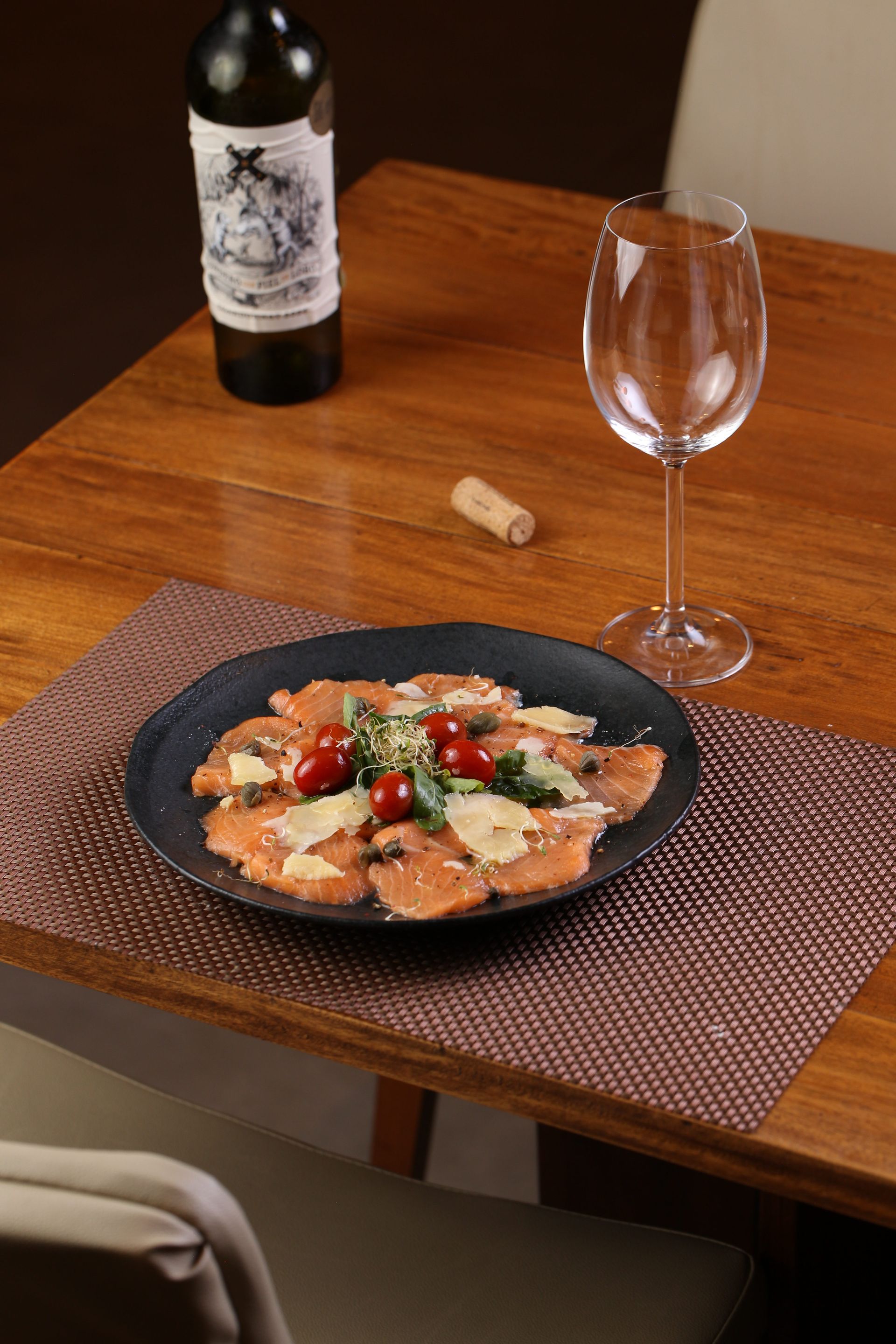 Um prato de comida está sobre uma mesa ao lado de uma taça de vinho e uma garrafa de vinho.