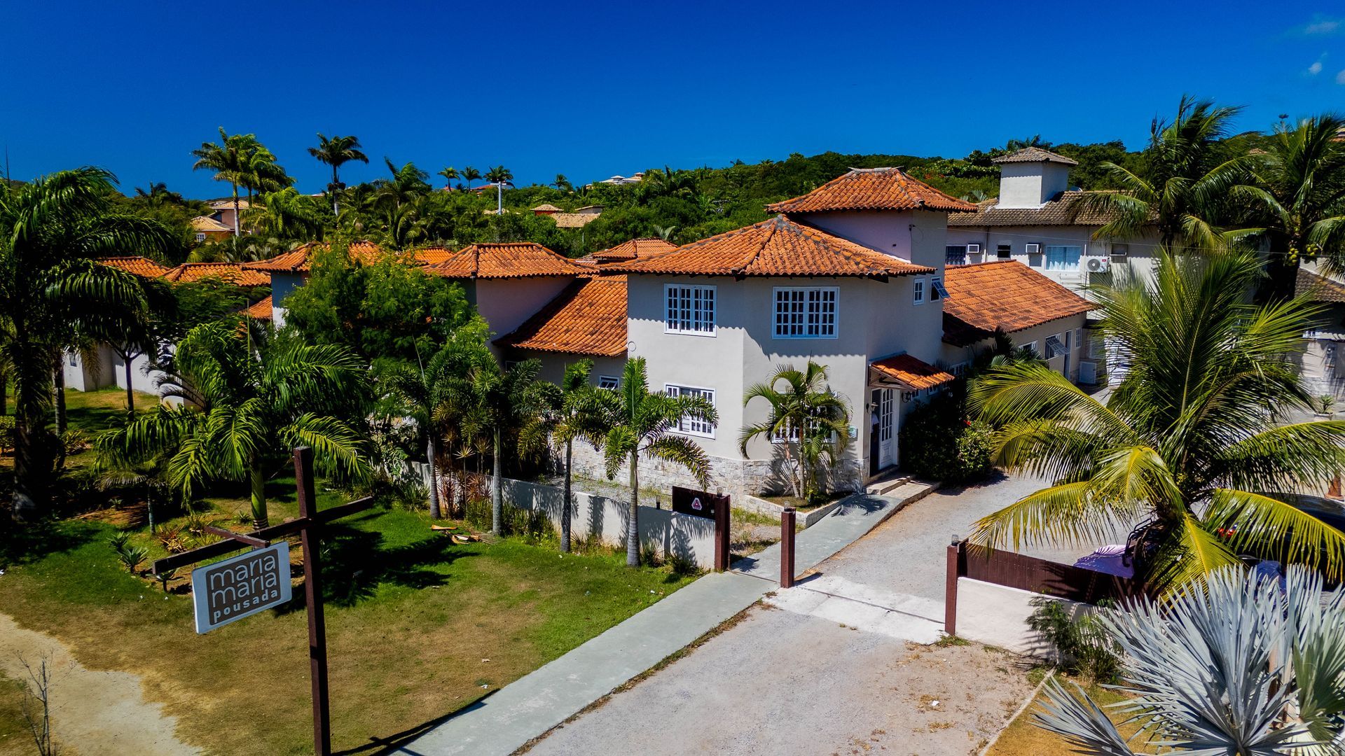 Uma vista aérea de uma grande casa branca com um telhado de telhas vermelhas cercada por palmeiras.