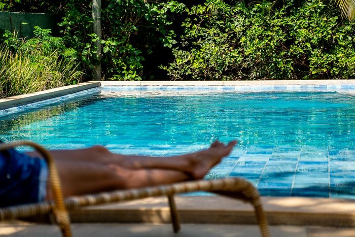 Uma pessoa está deitada em uma espreguiçadeira ao lado de uma piscina.