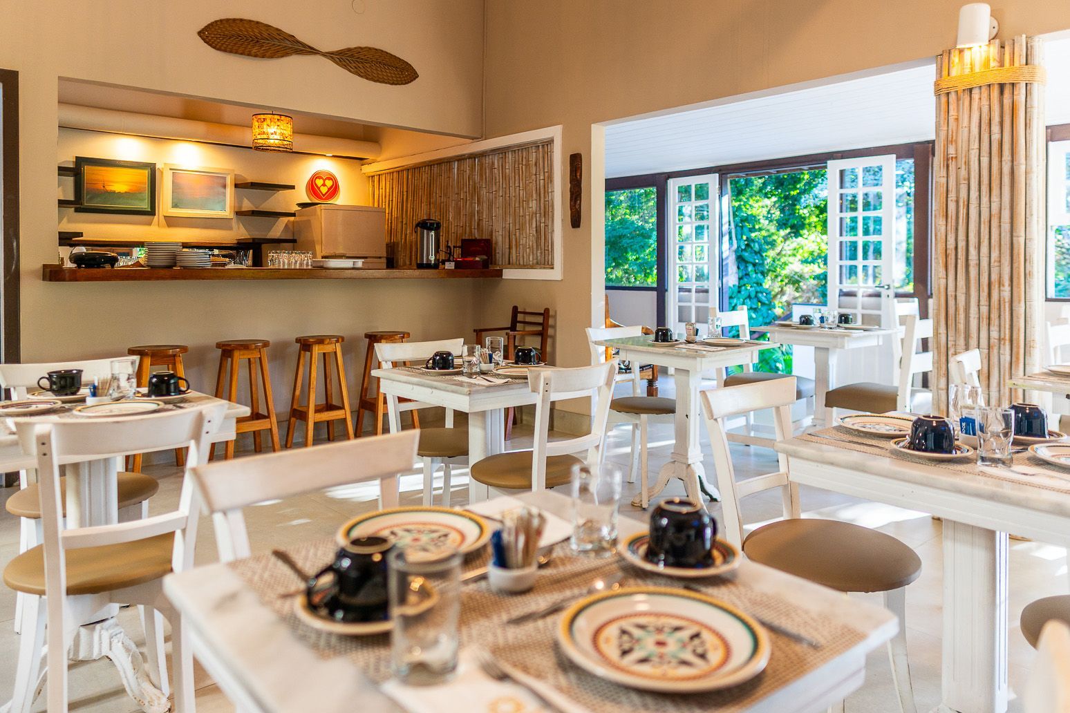 Uma sala de jantar com mesas e cadeiras preparadas para uma refeição.
