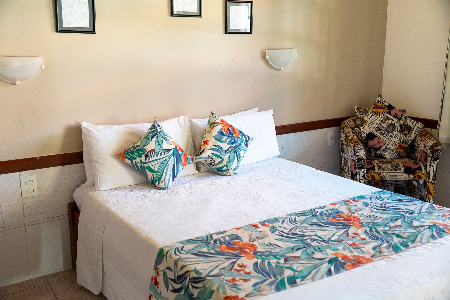 Um quarto de hotel com uma cama, cadeira e quadros na parede.
