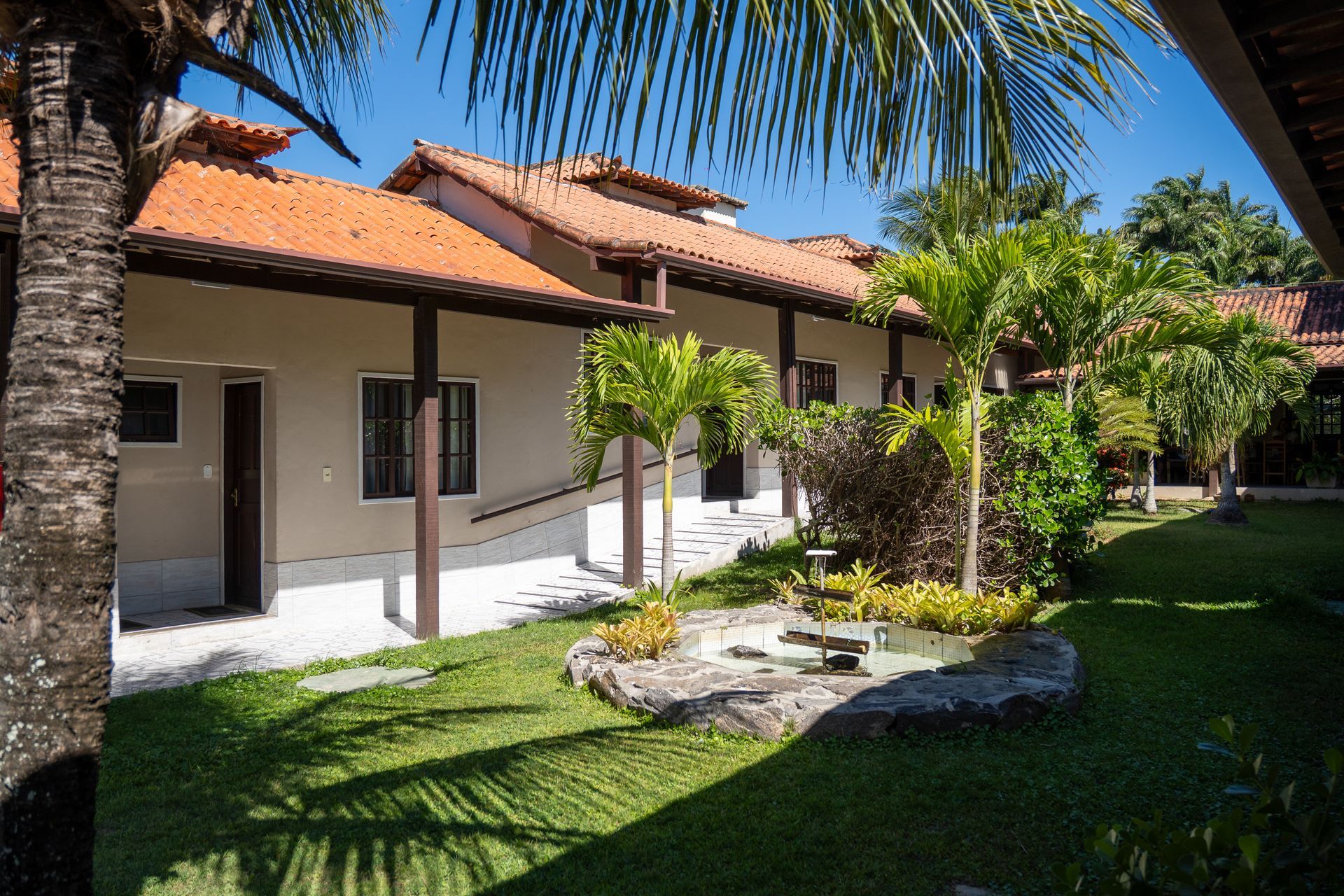 Uma casa com telhado de telha vermelha é cercada por árvores e grama.