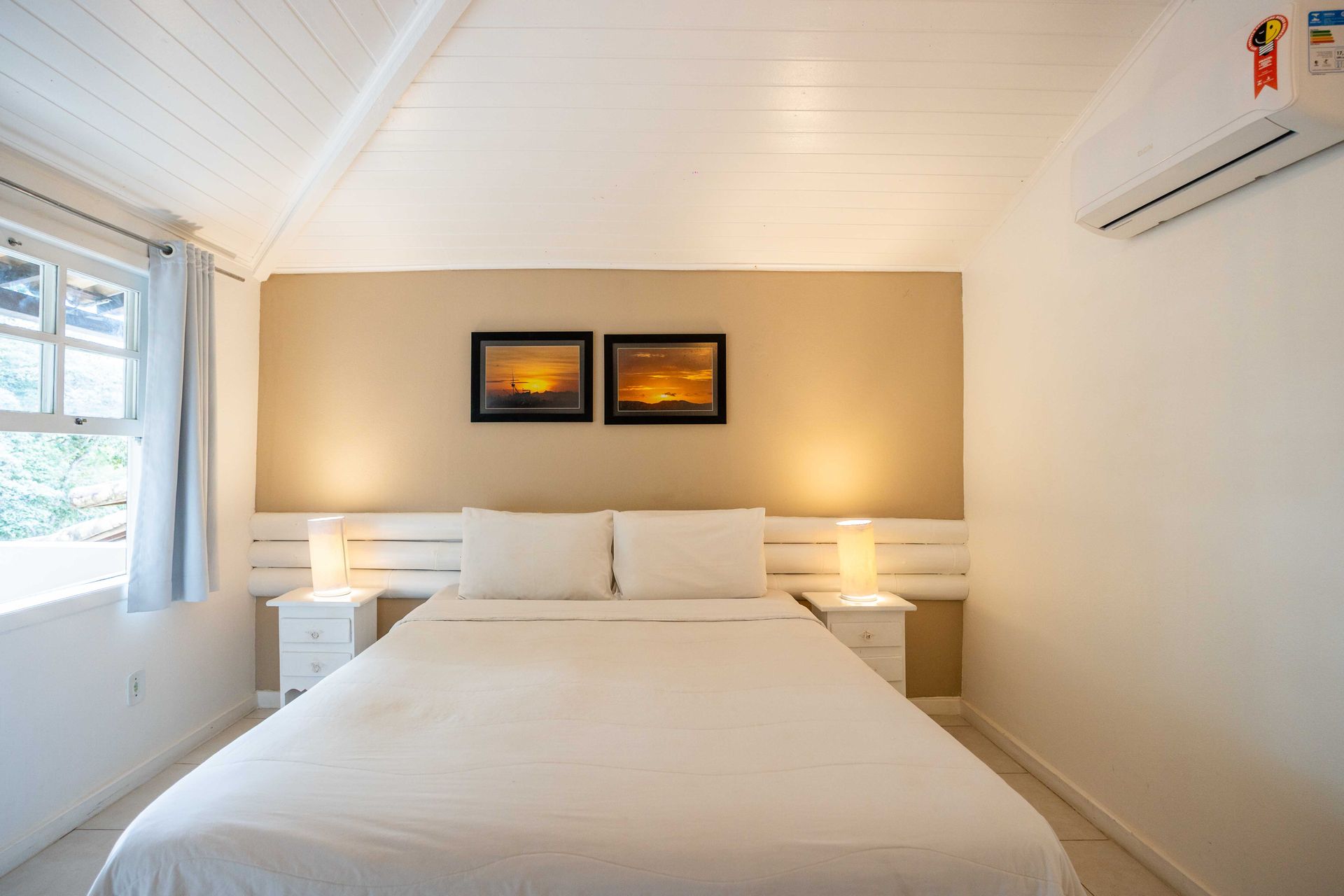 Um quarto com uma cama, duas mesas de cabeceira e dois quadros na parede.