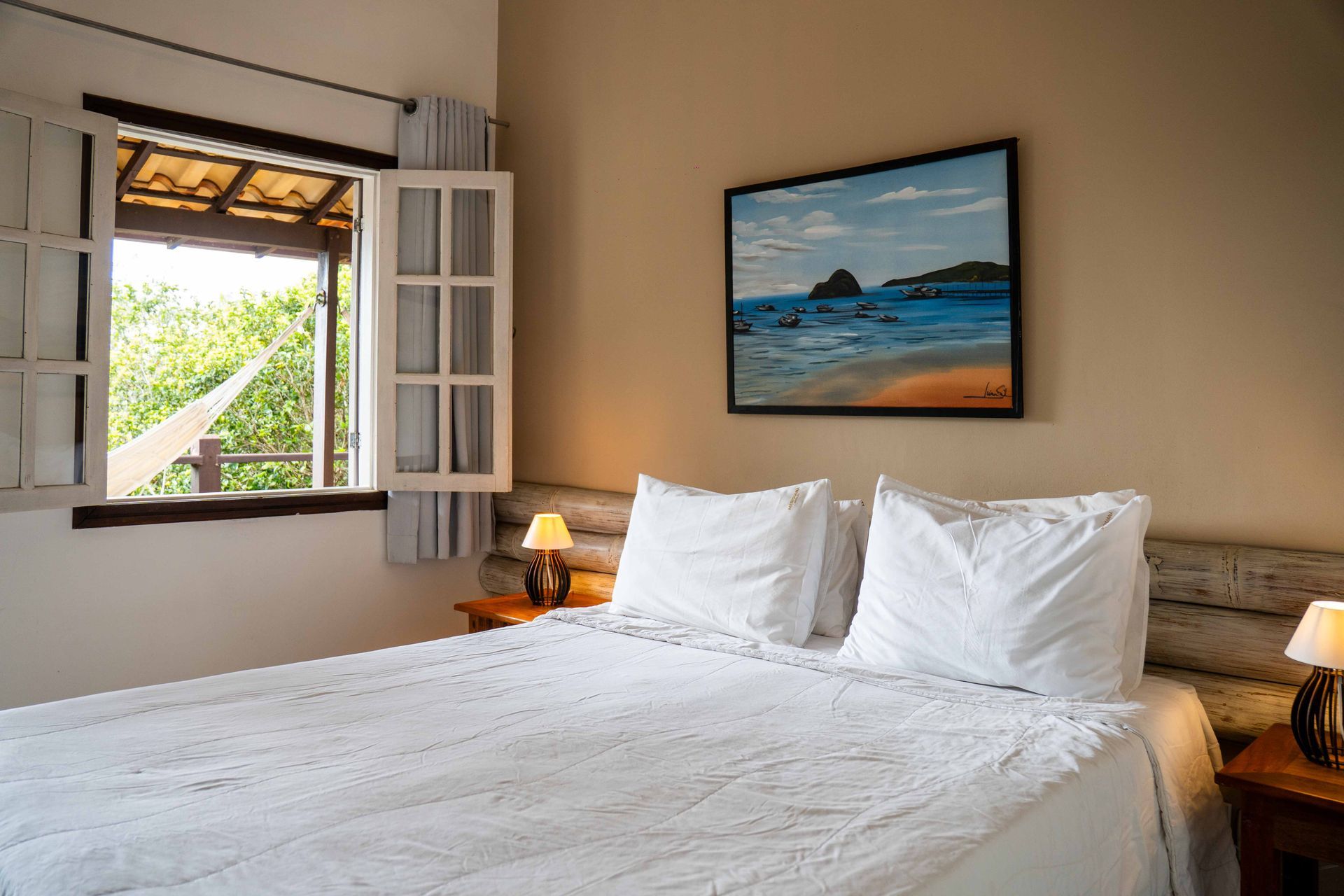 Um quarto com cama king size com um quadro acima da cama e uma vista da janela para a varanda. 