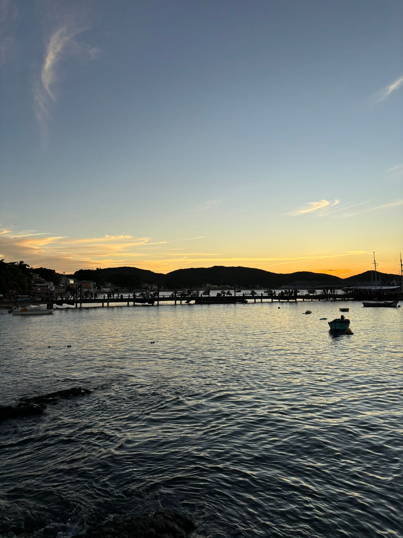 Um pôr do sol sobre um corpo de água com uma ponte ao fundo.