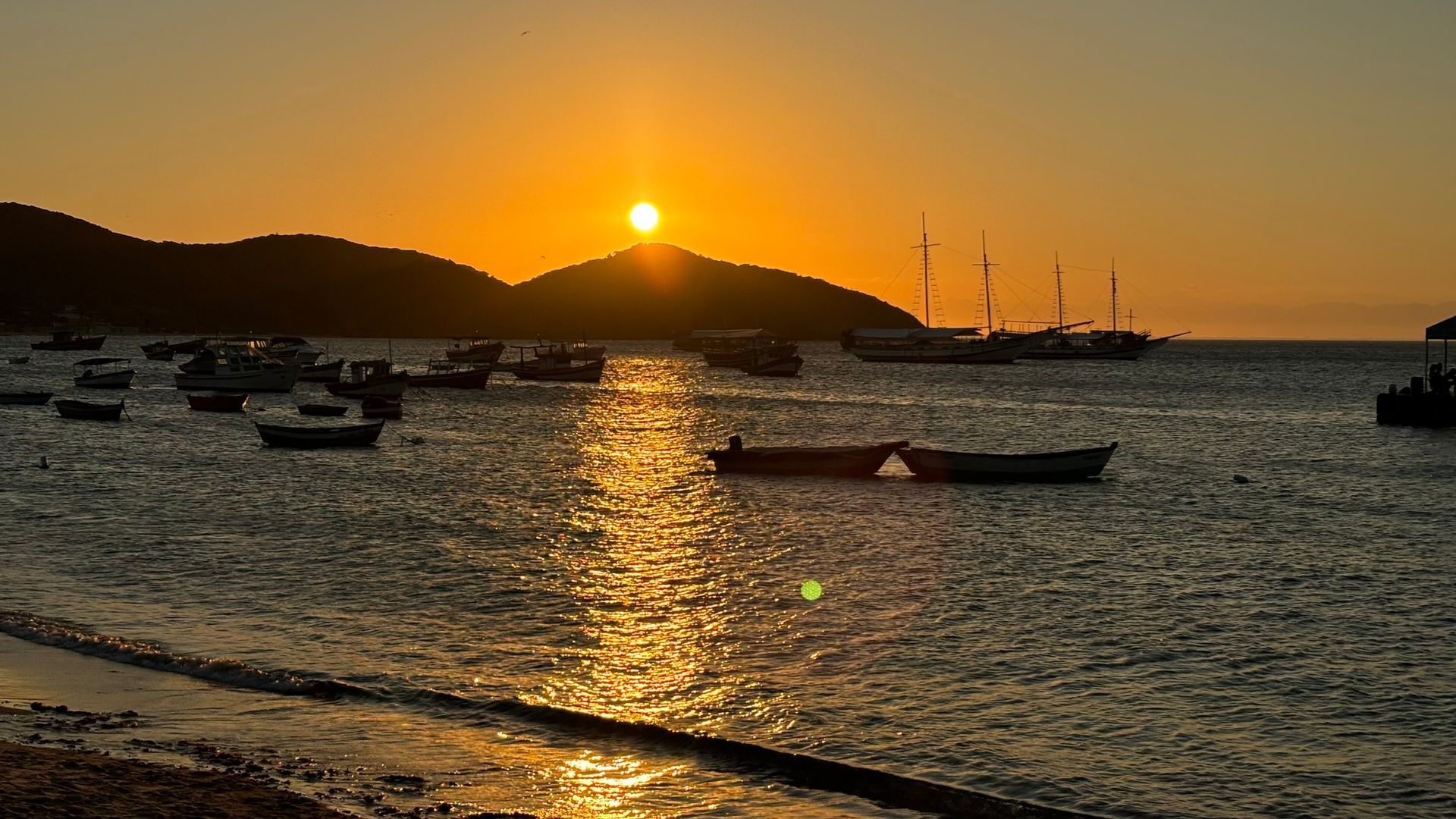 O sol está se pondo sobre o oceano com barcos na água.