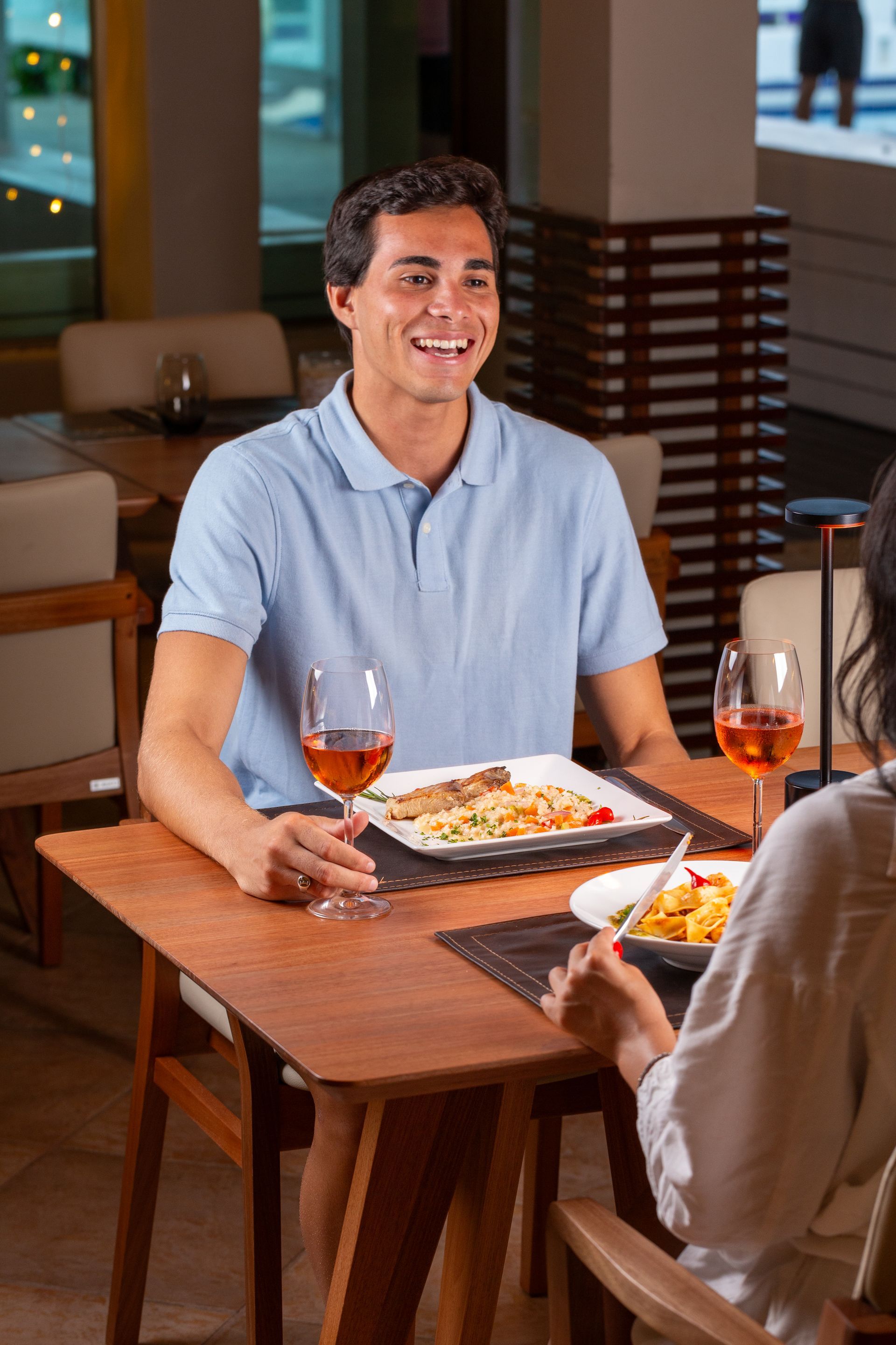 Um homem e uma mulher estão sentados à mesa de um restaurante comendo e bebendo vinho.