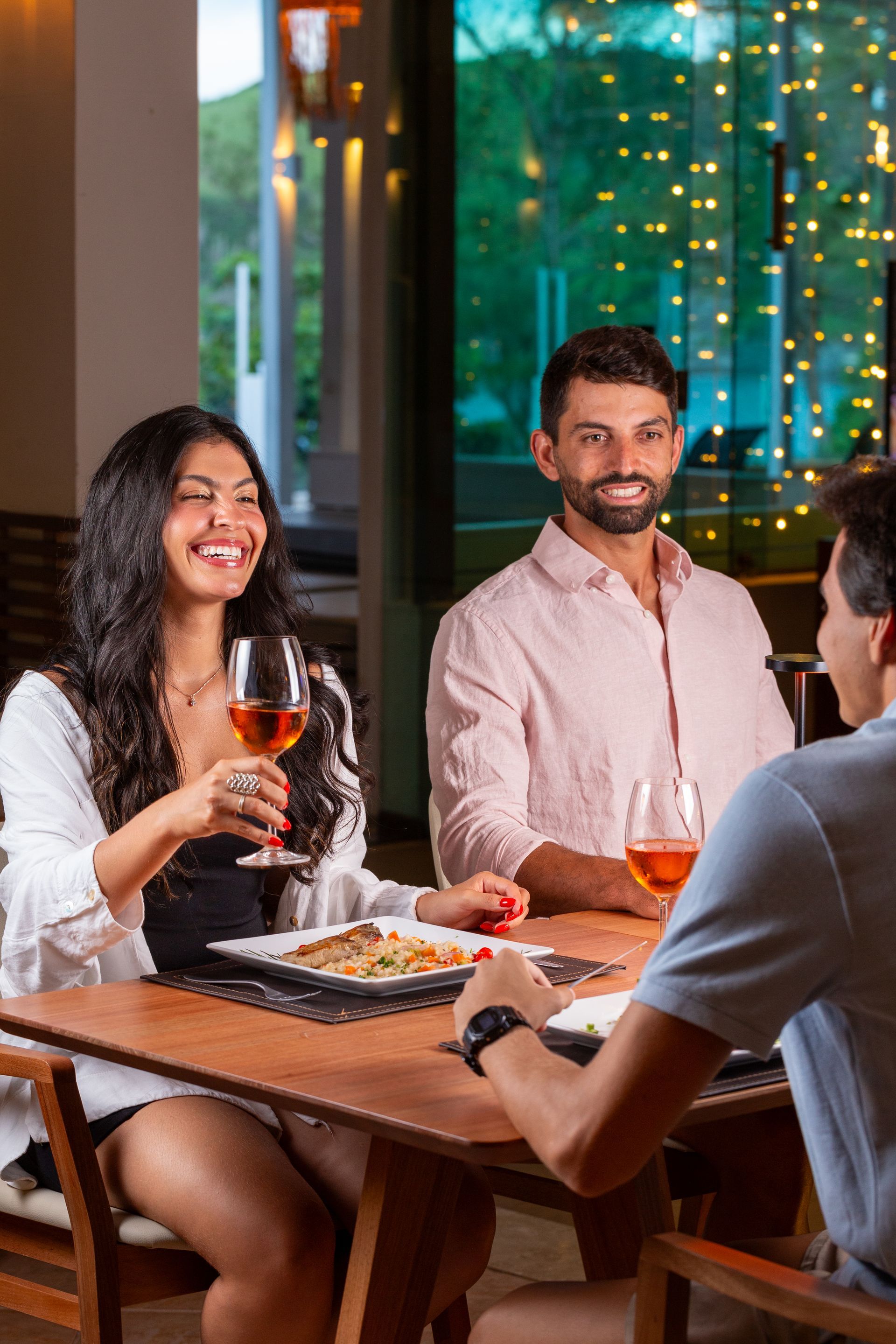 Um grupo de pessoas está sentado à mesa comendo e bebendo vinho.