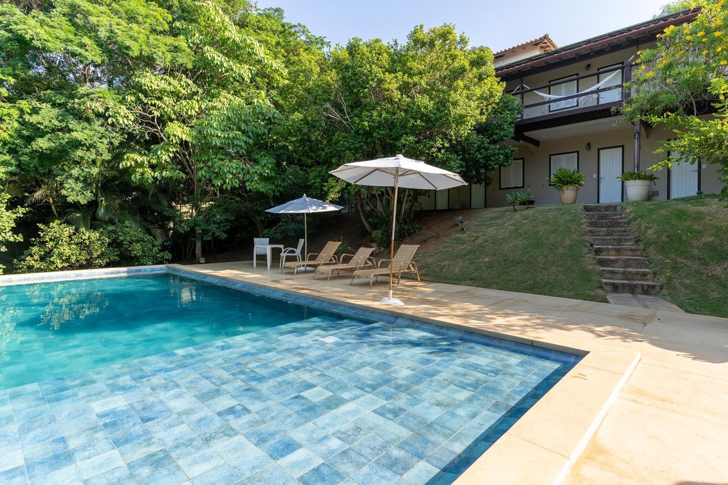 Uma grande piscina cercada por cadeiras e guarda-sóis em frente a uma casa.