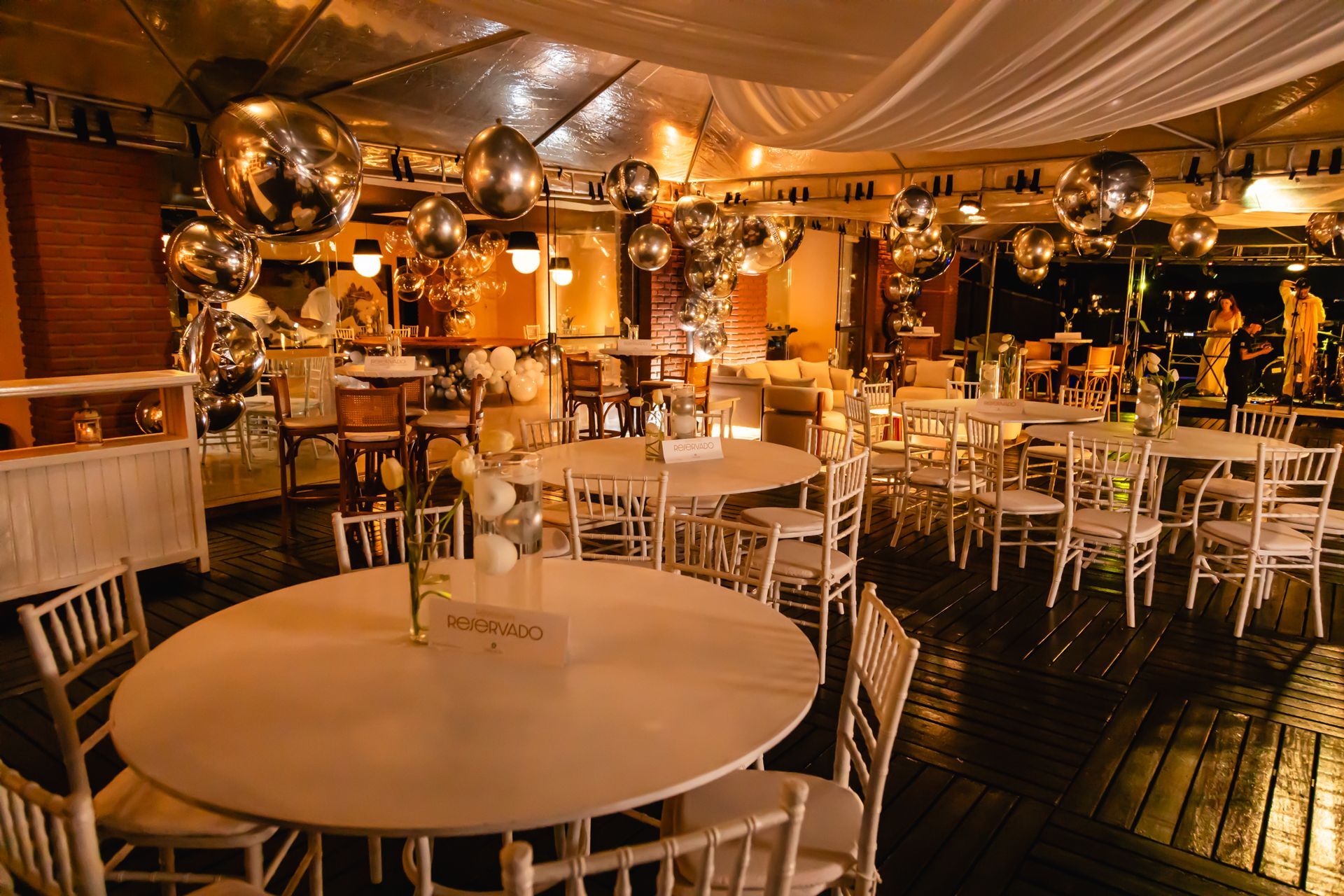 Round tables with white chairs in a decorated event space, lit with overhead lights and disco balls.