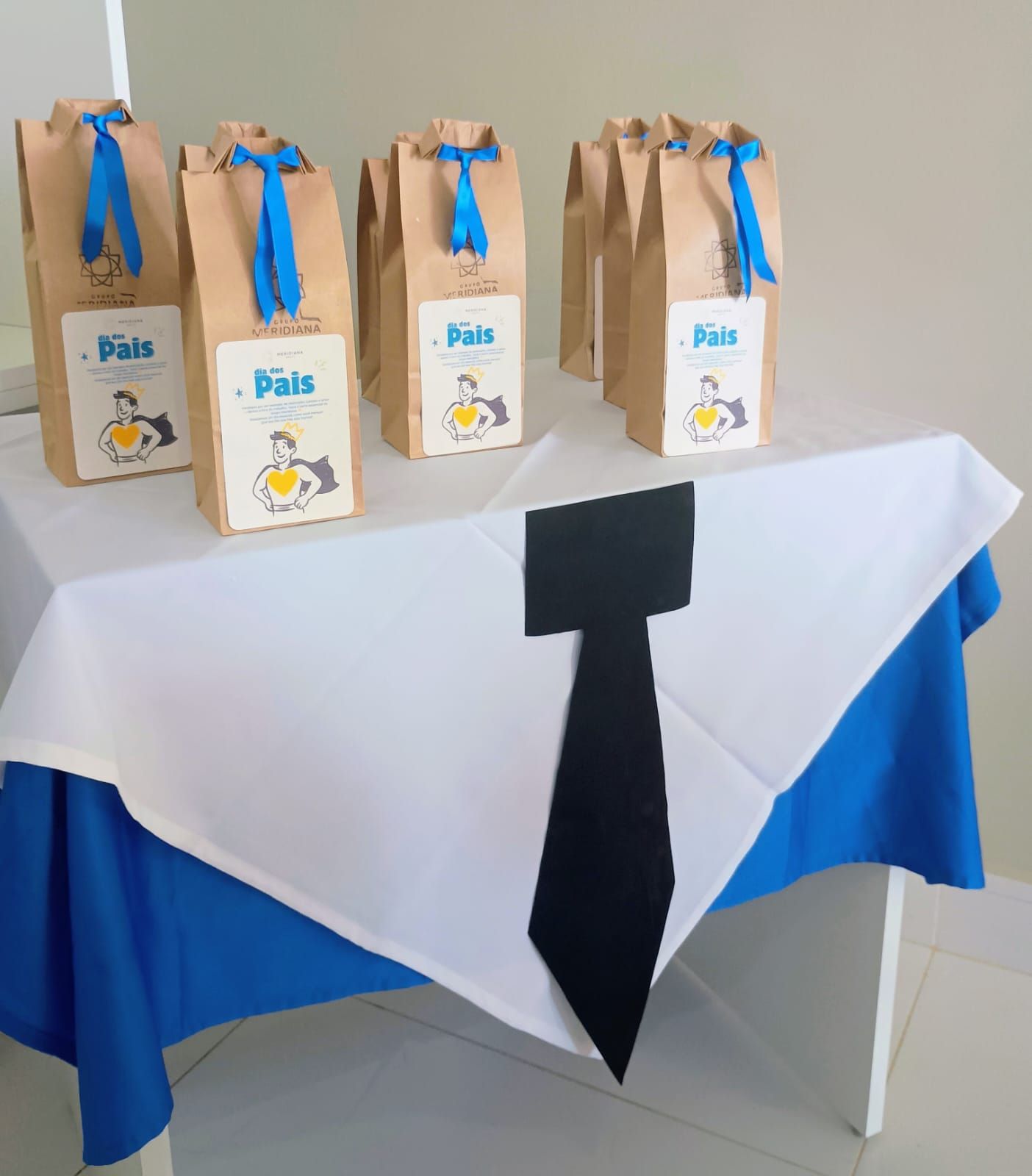 Gifts in brown paper bags with blue ribbon on a table decorated as a shirt for Father's Day.