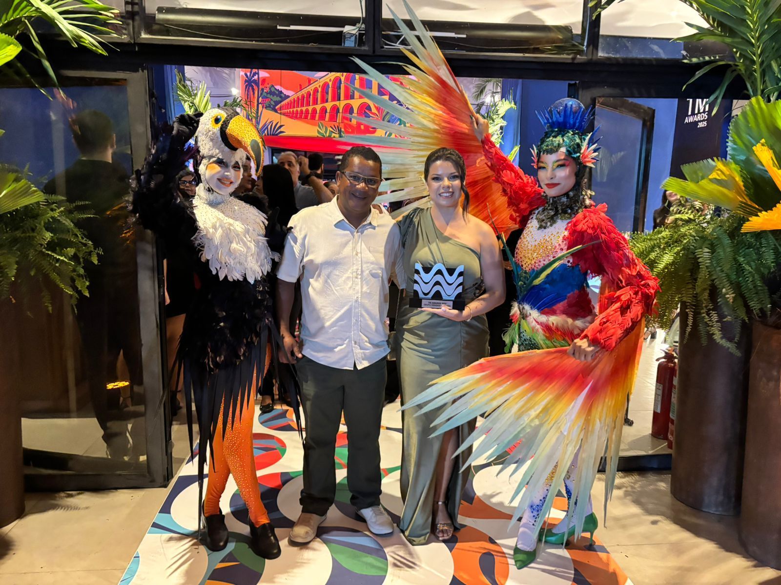 Pessoas posam para fotos com artistas fantasiados em um evento; ambiente interno com decoração colorida.