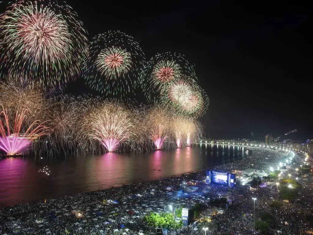 Uma grande multidão de pessoas está assistindo aos fogos de artifício sobre o oceano.
