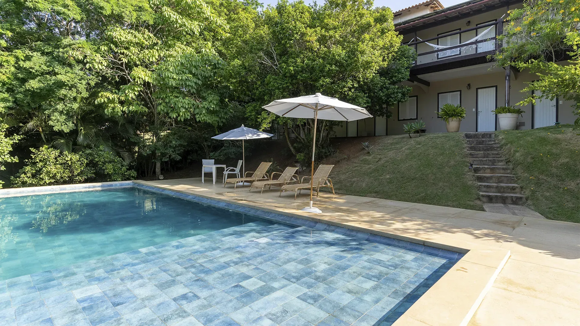 Uma grande piscina com cadeiras e guarda-sóis em frente a uma casa
