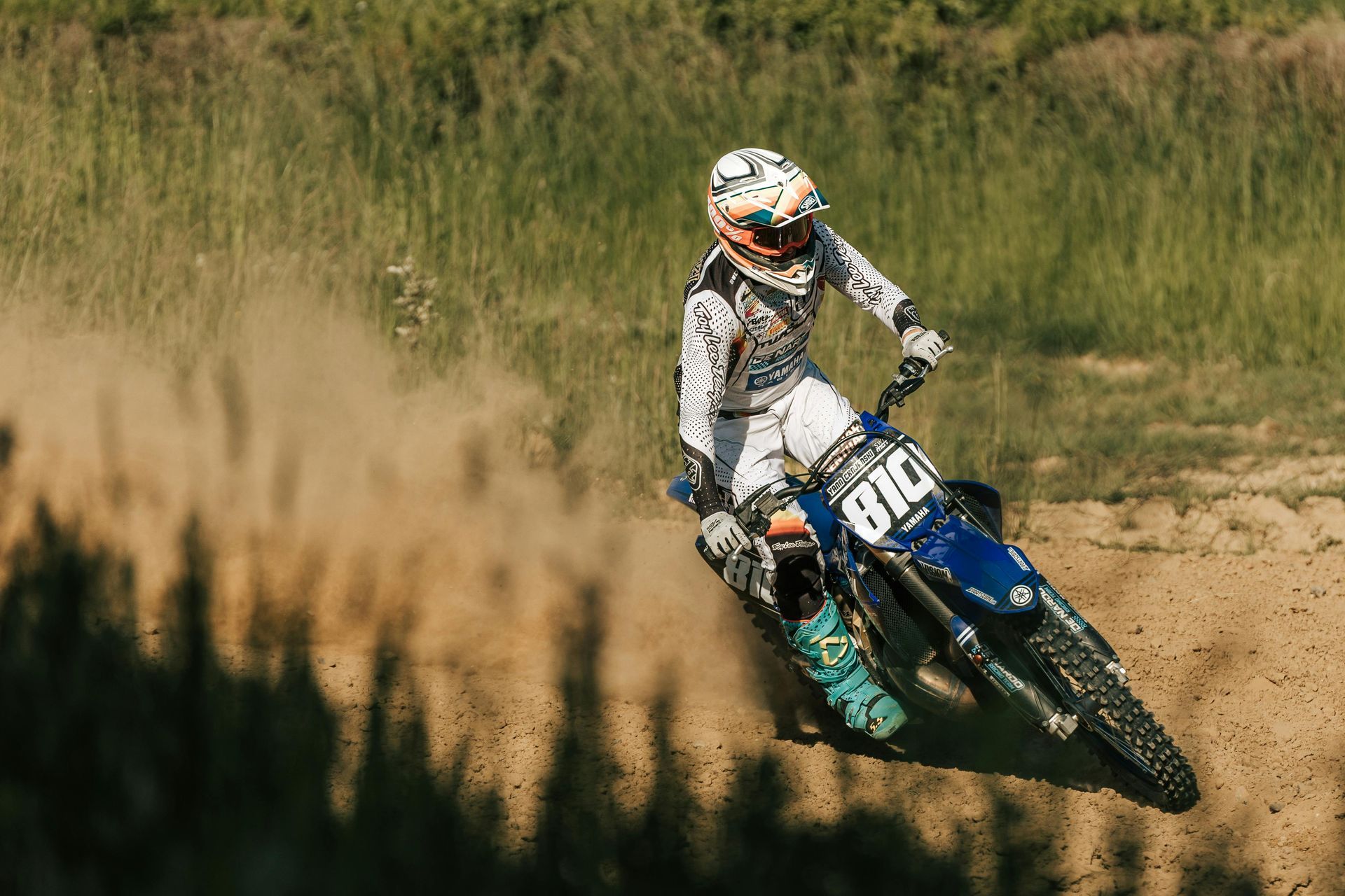 Piloto de motocross em uma motocicleta azul e branca levantando poeira na pista.