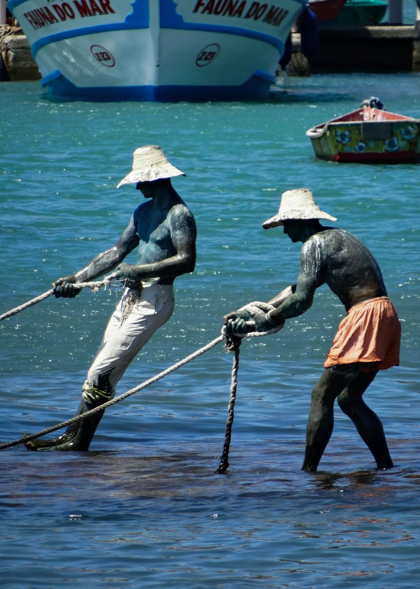 Dois homens puxam uma corda na água com um barco ao fundo que diz pauna do mar