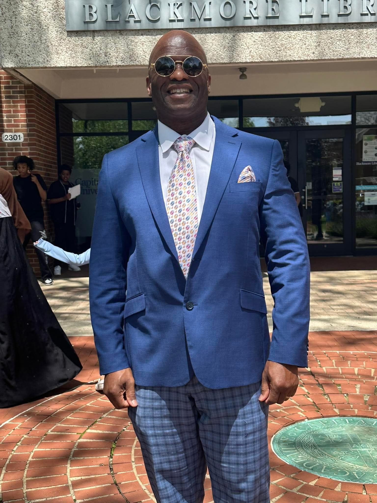 A man in a blue suit and tie is standing in front of a building.