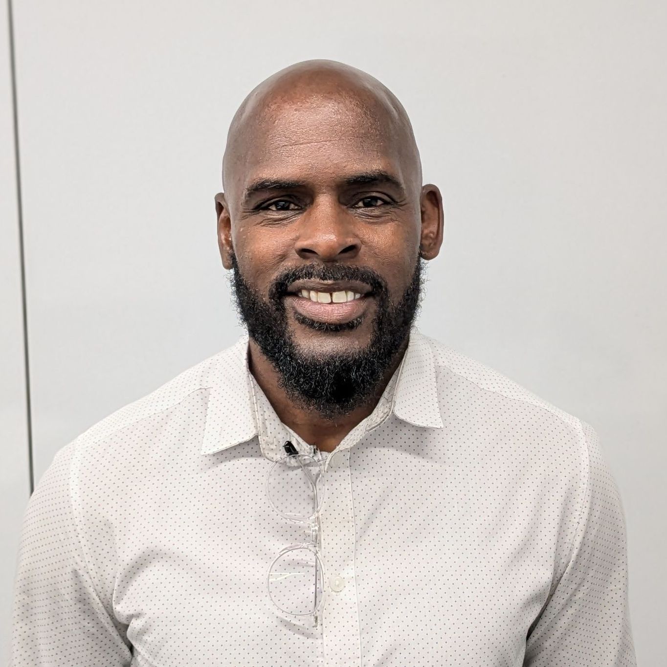 A bald man with a beard is wearing a white shirt and smiling.