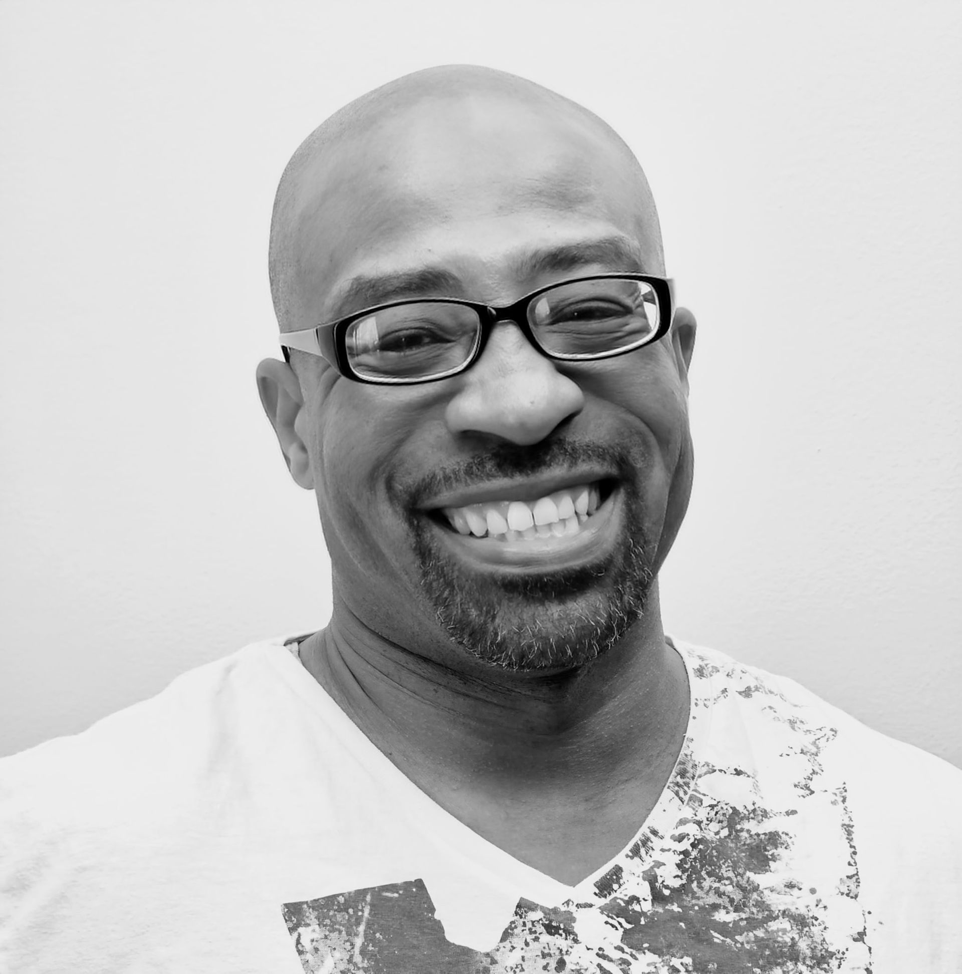A man with glasses and a beard is smiling in a black and white photo.