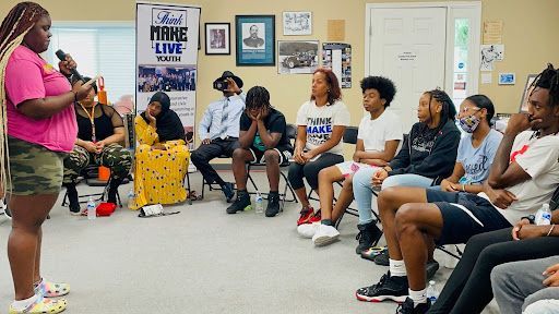 A woman is standing in front of a group of people sitting in chairs.