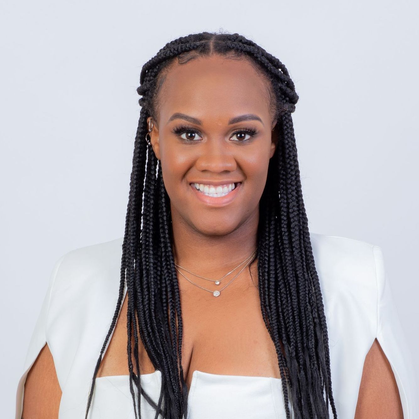 A woman with braids is wearing a white dress and a white cape.