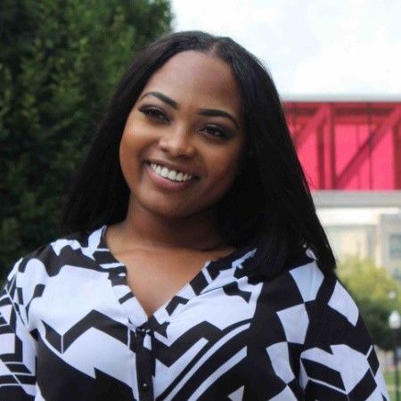 A woman in a black and white shirt is smiling in front of a red bridge.