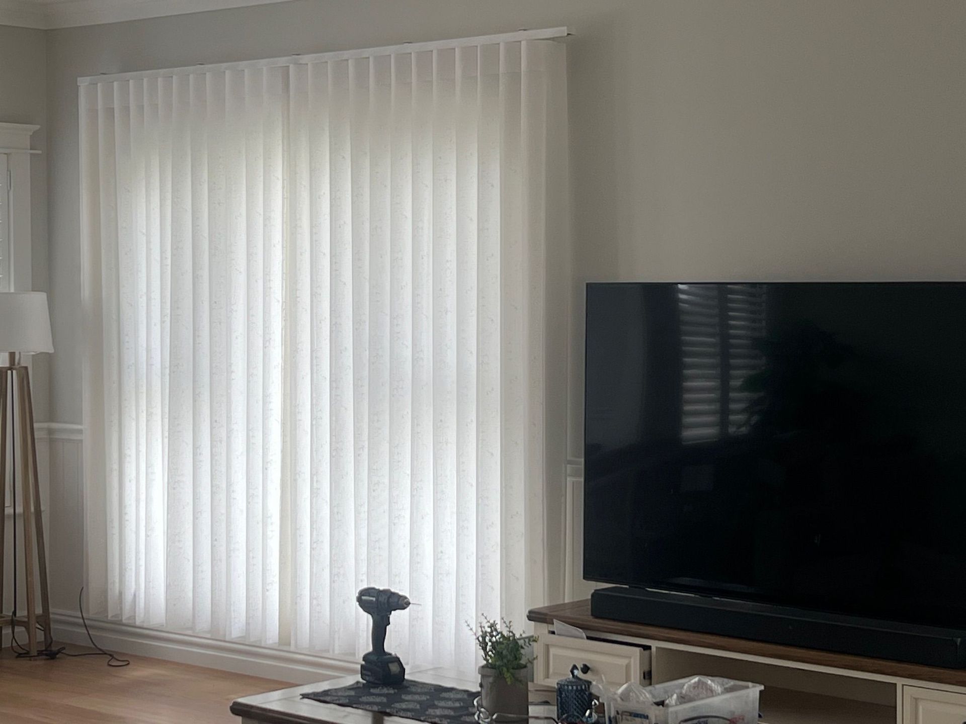 A living room with white vertical blinds and a flat screen tv.