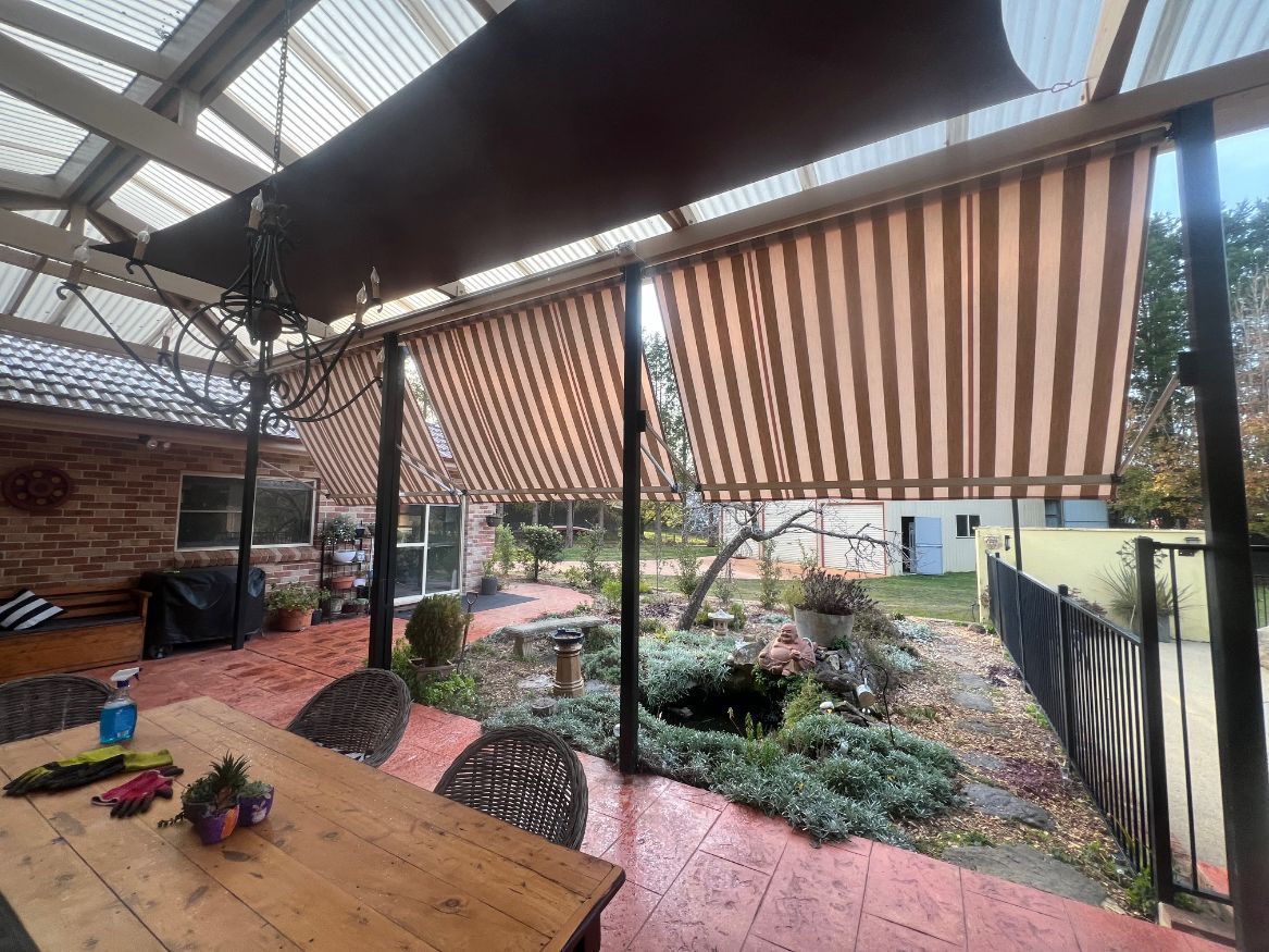 A wooden table and chairs under a striped awning on a patio.