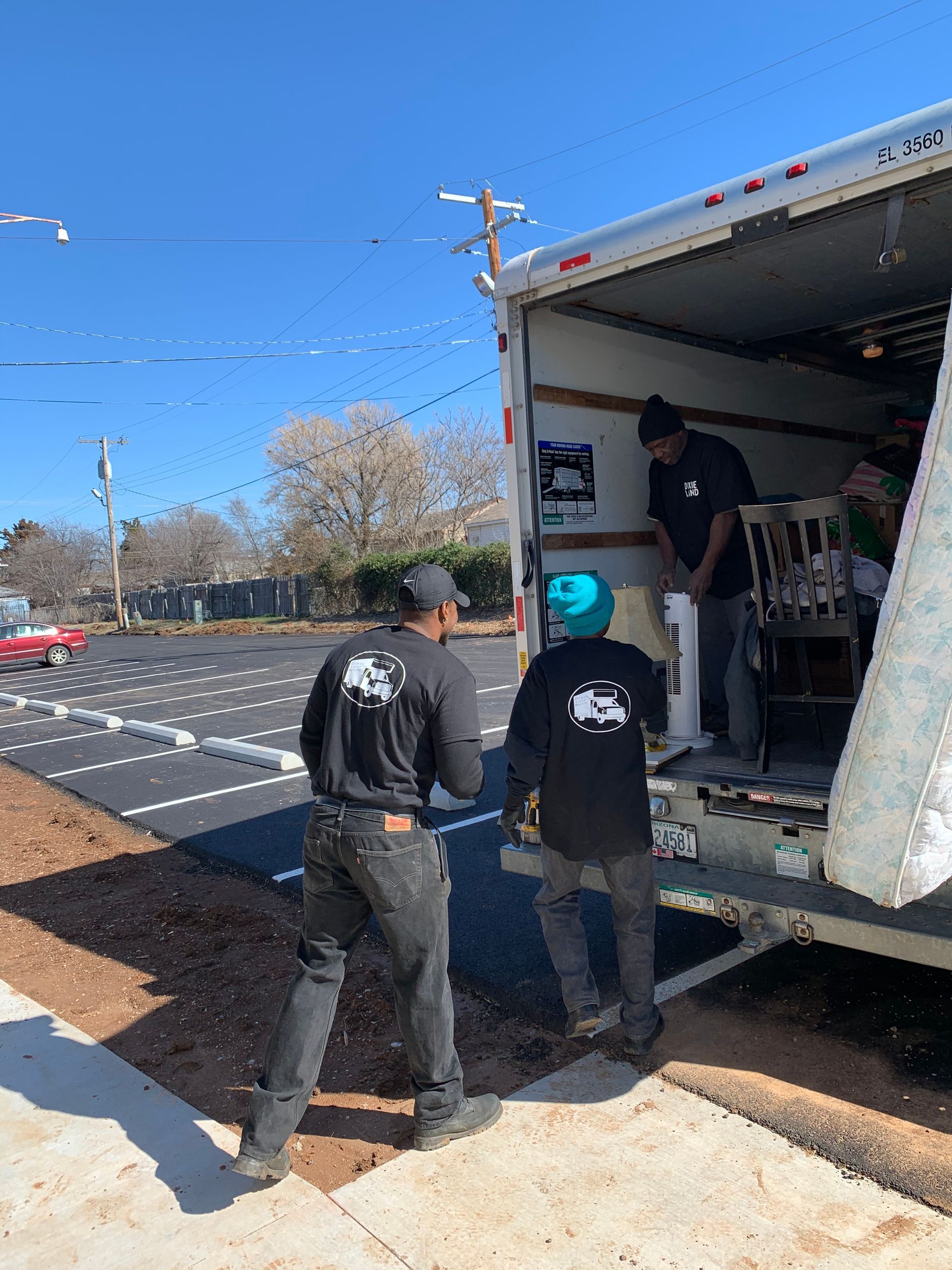 Woman on couch in apartment, using phone, surrounded by stacked moving boxes, window view.