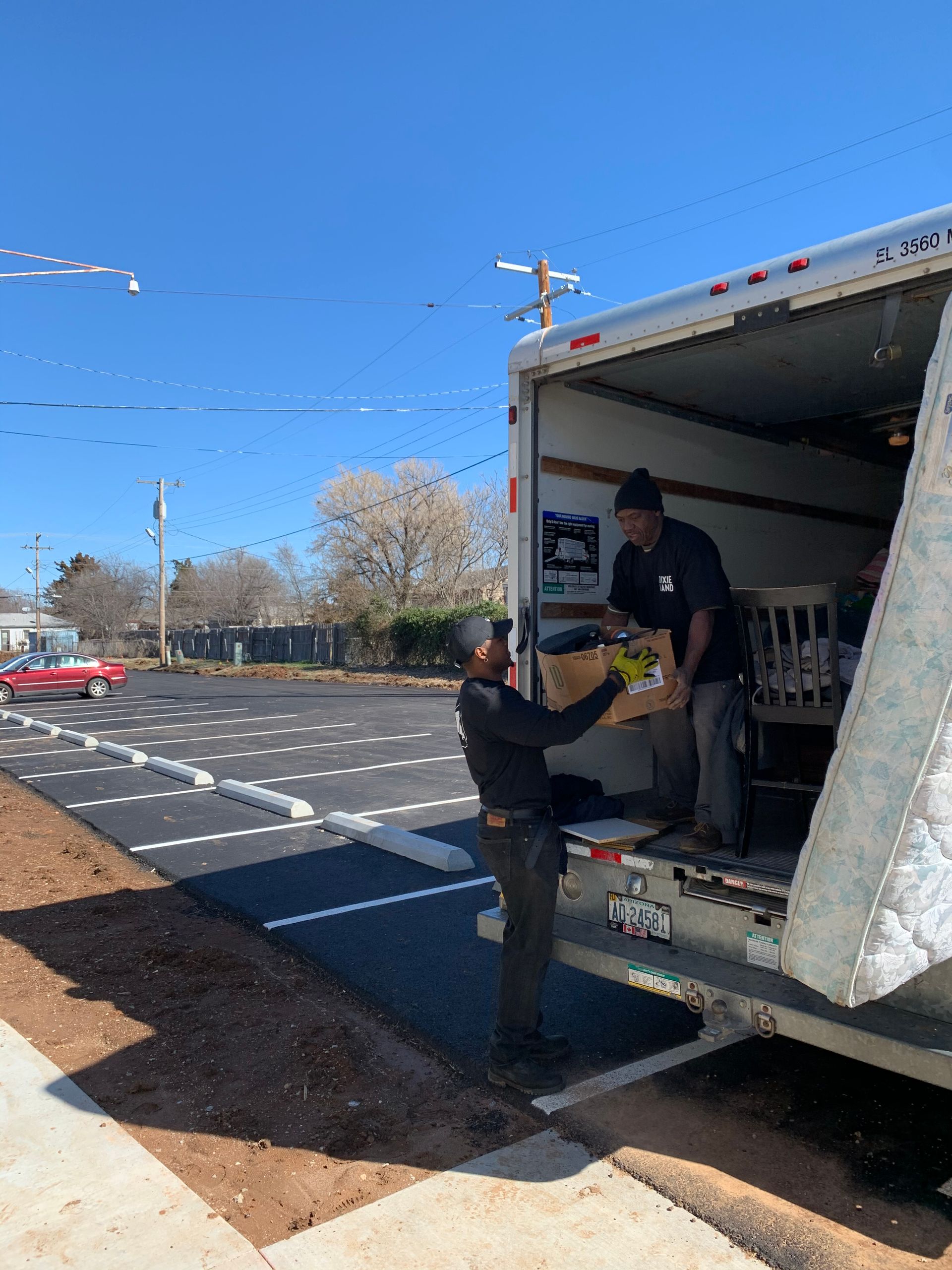Two men loading a wrapped piano onto a truck from a dolly on a residential street.