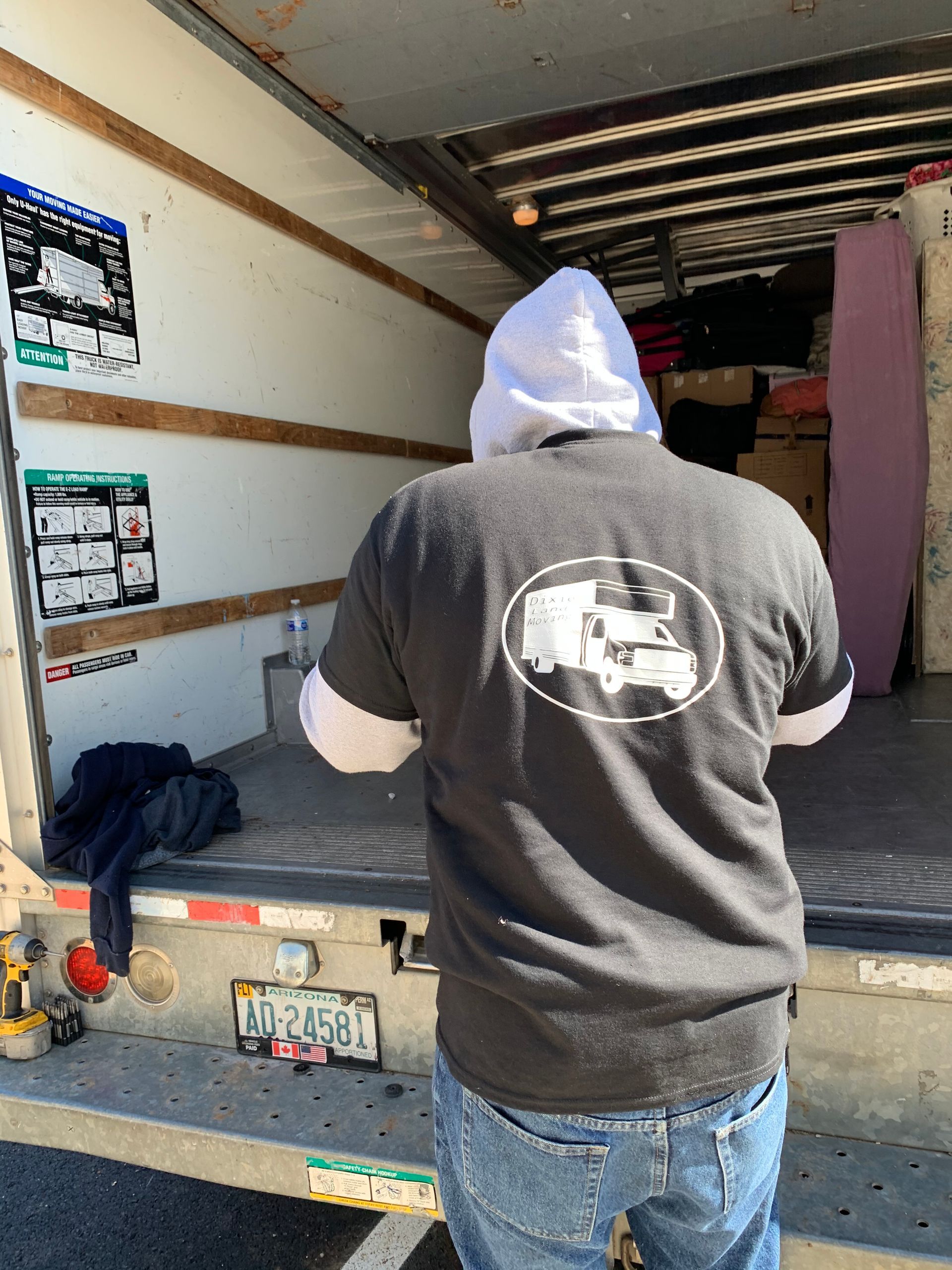A person wearing a gray hoodie and t-shirt stands at the back of an open moving truck, facing inside.