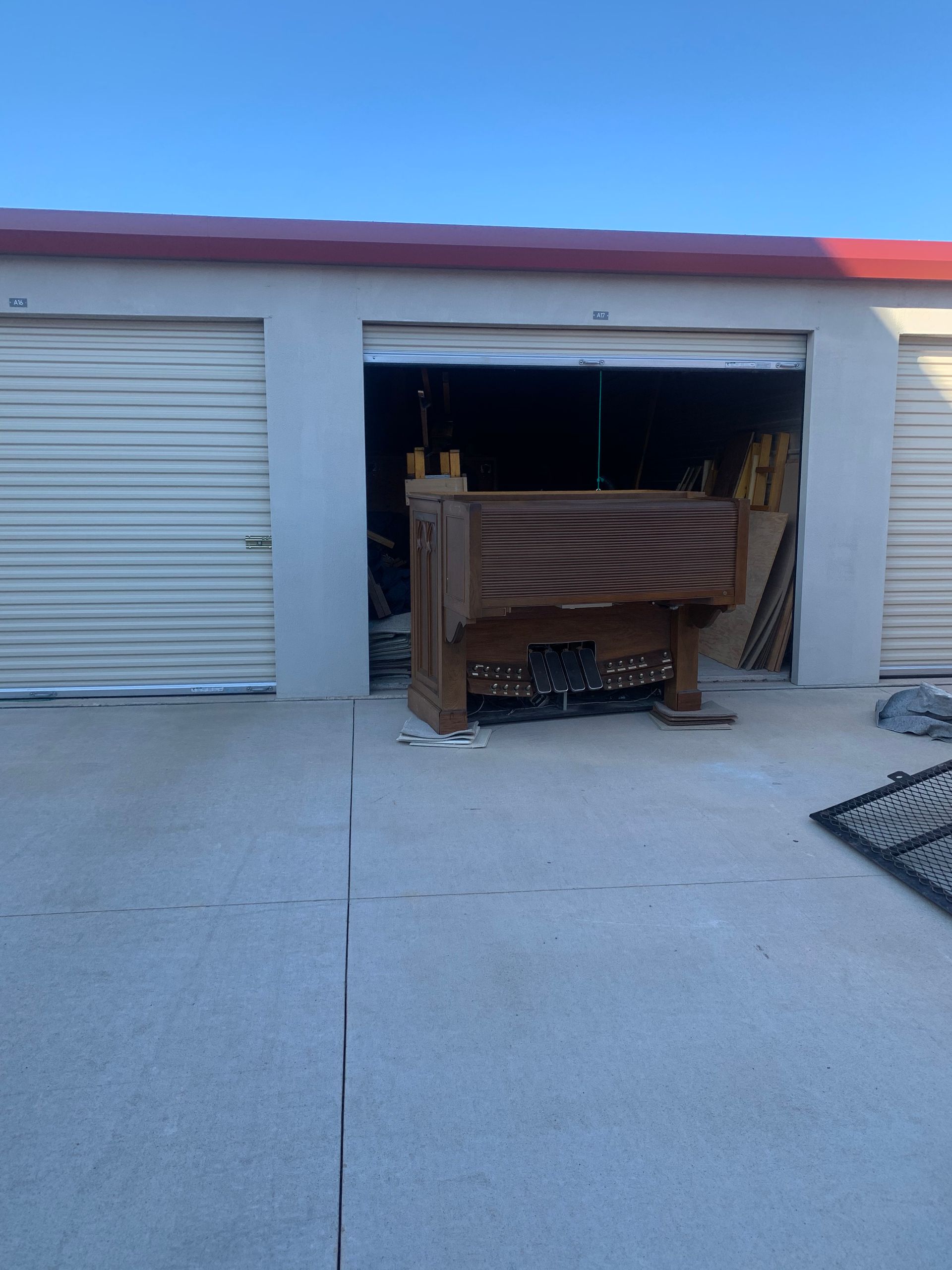 A brown wooden vanity or cabinet sits in the open doorway of a concrete storage unit under a bright blue sky.