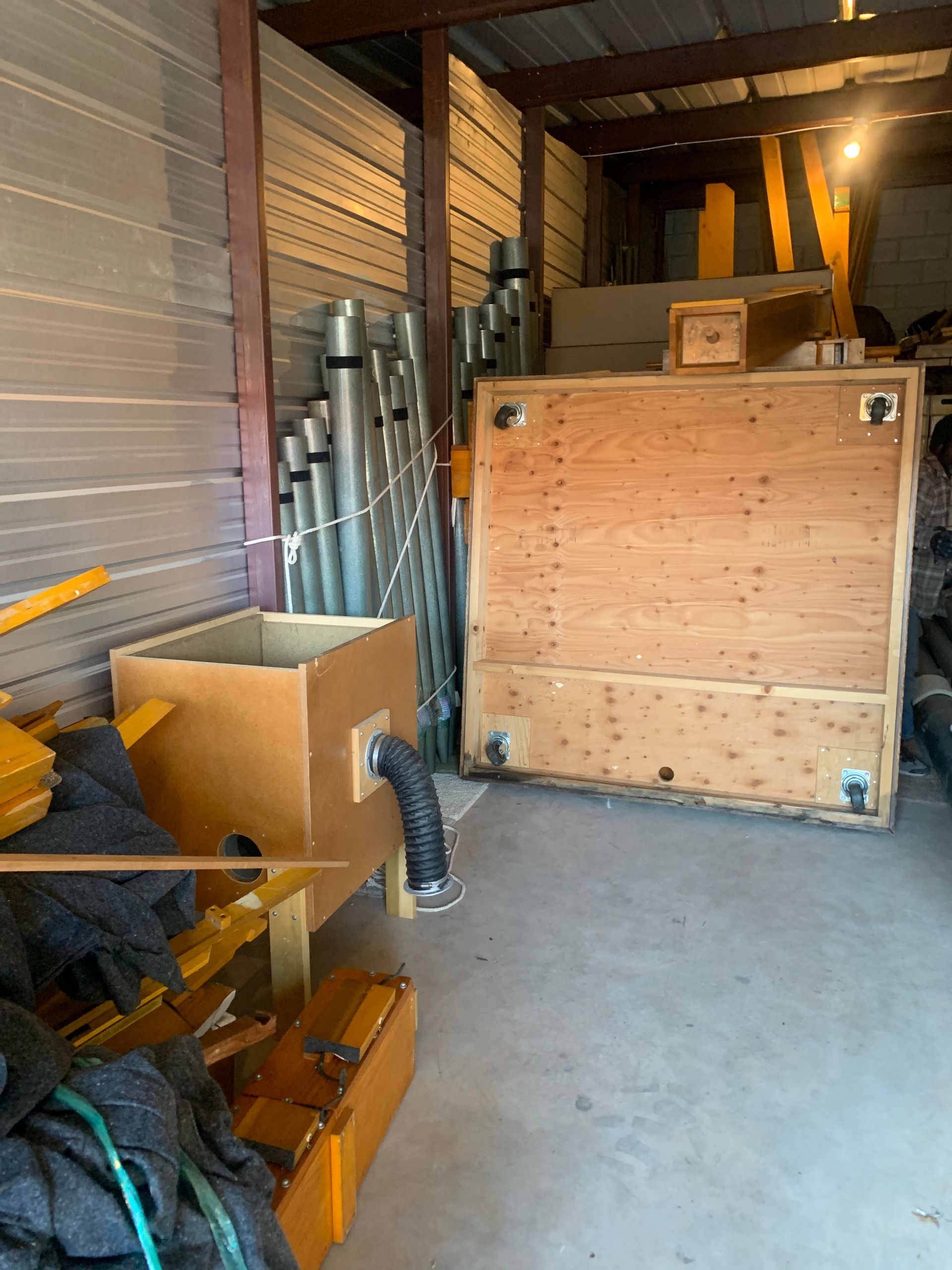 A storage unit containing a large wooden crate, metal pipes, and a cardboard box with a flexible hose attachment.