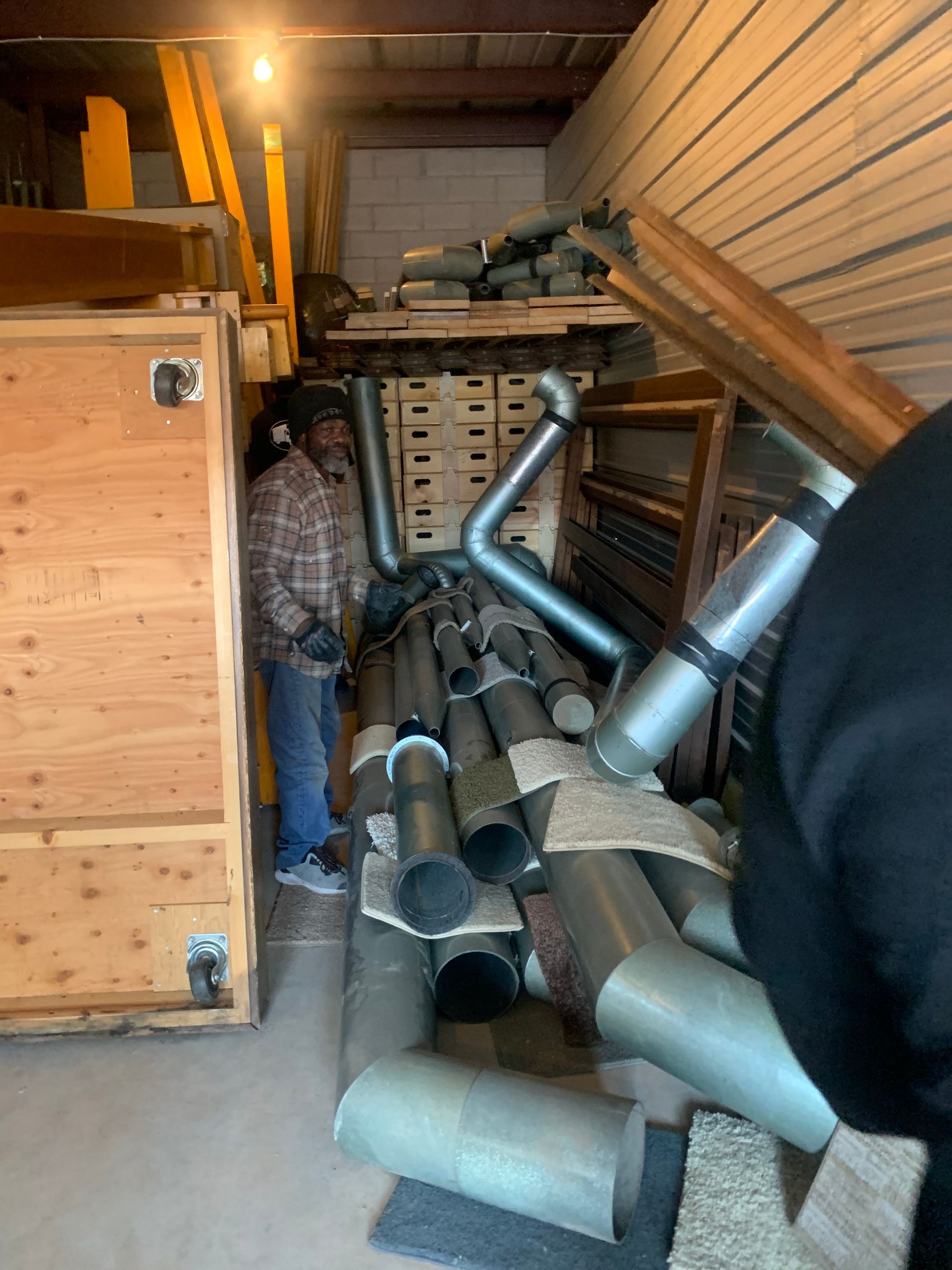 A person stands in a storage unit filled with metal ductwork and wooden crates.