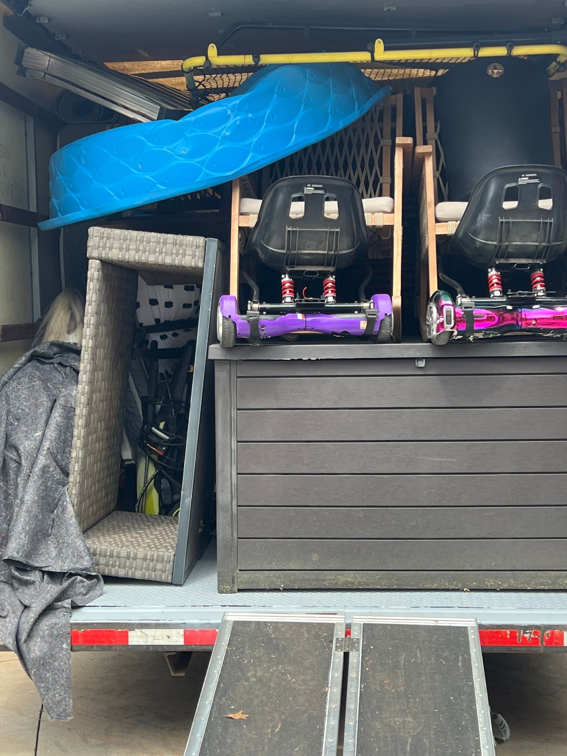 The back of a moving truck packed with furniture, including a large plastic storage trunk, two hoverboard karts, and a pool.
