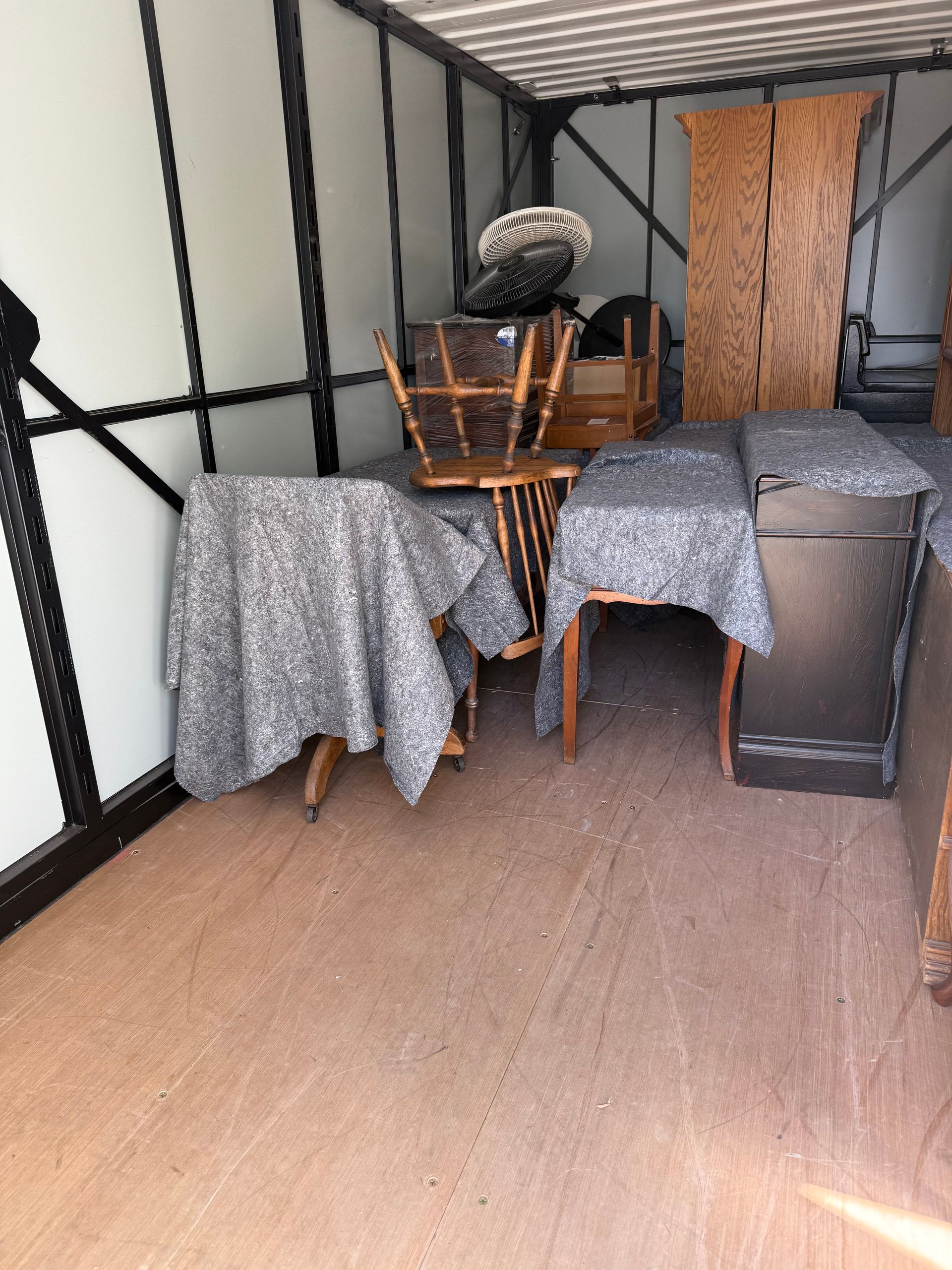Furniture including chairs, a table, and a tall cabinet packed inside a storage container or moving truck.