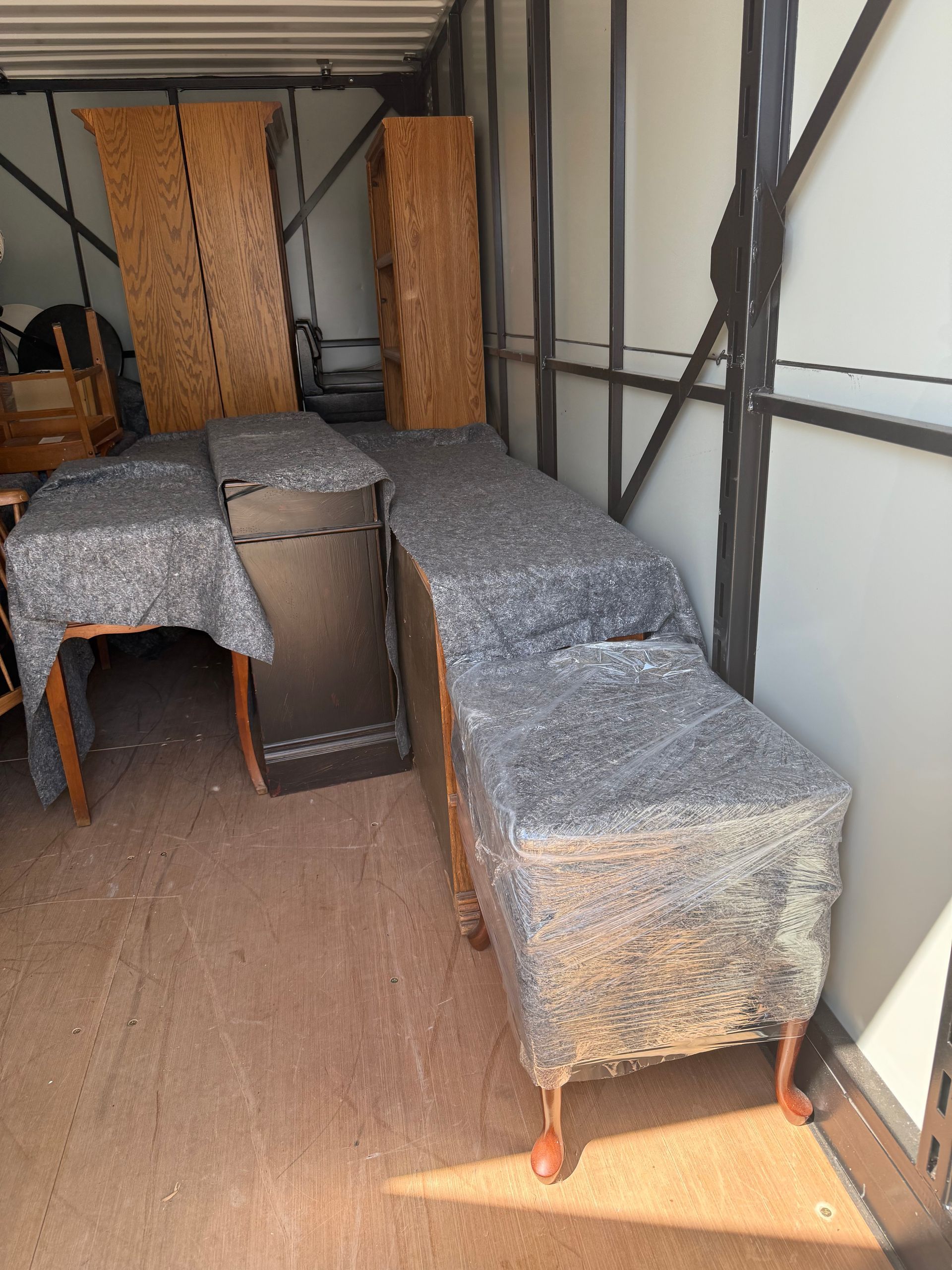 Furniture wrapped in protective blankets and plastic is arranged inside a moving truck.
