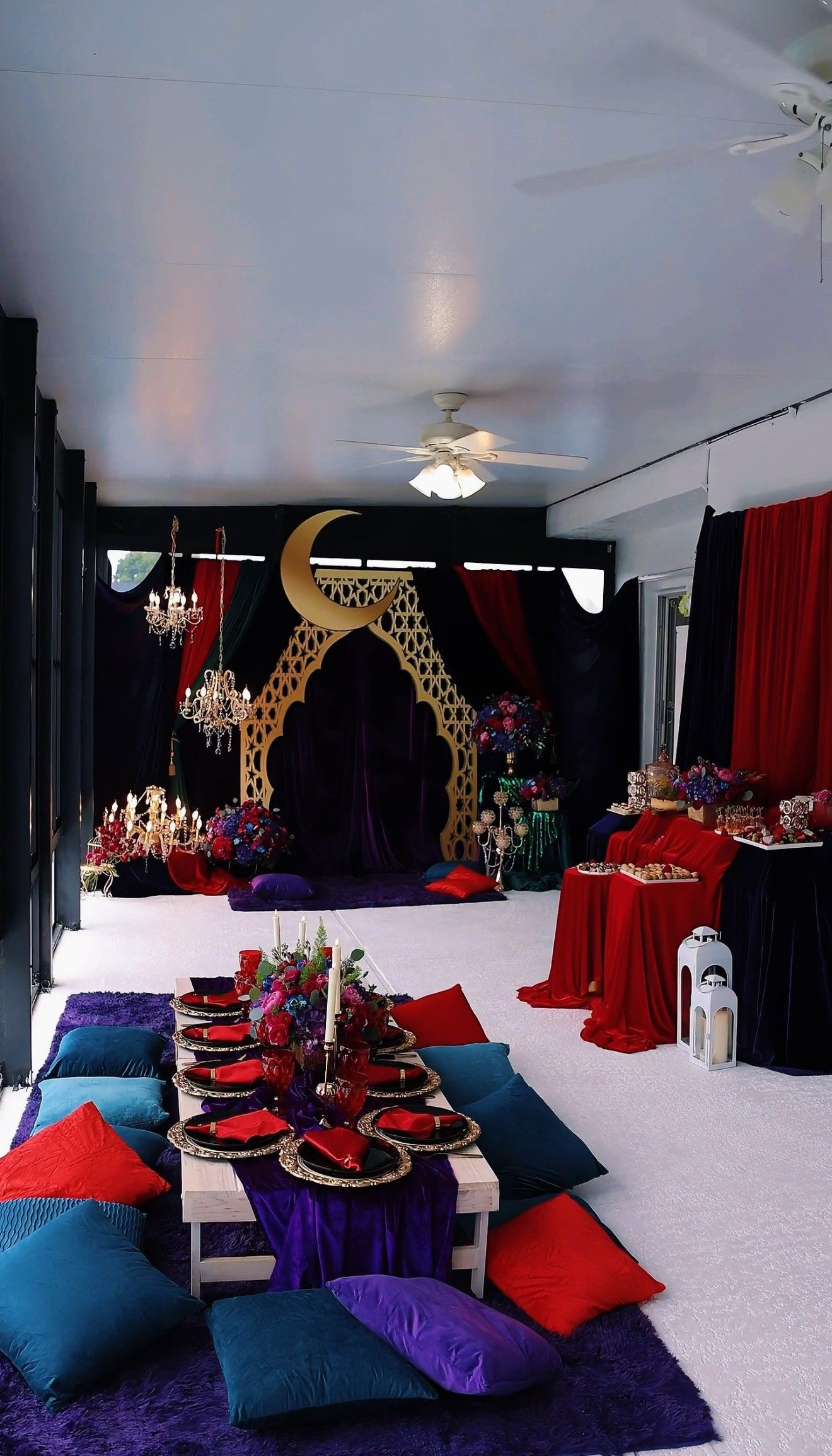 Table setting with purple accents, surrounded by pillows. Plates, flowers, candles, and gold cutlery.