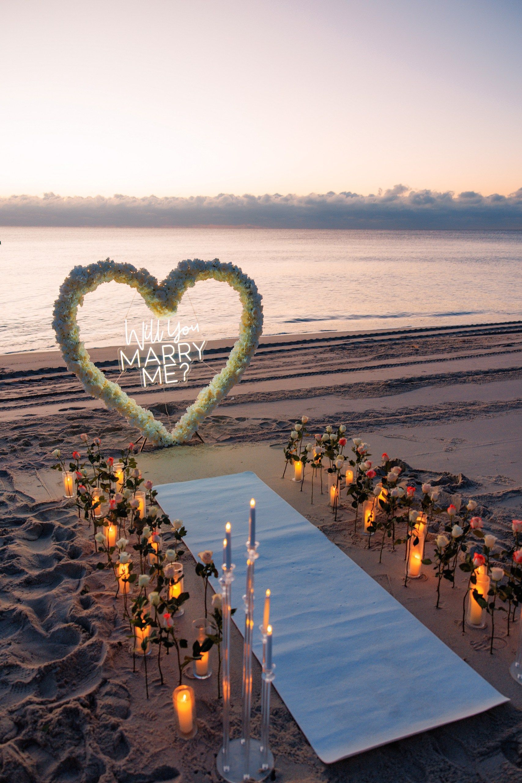 Beach proposal setup: Heart-shaped floral arch with 