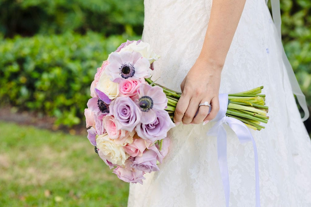 Bride in white dress holding a bouquet of pink, purple, and white flowers.
