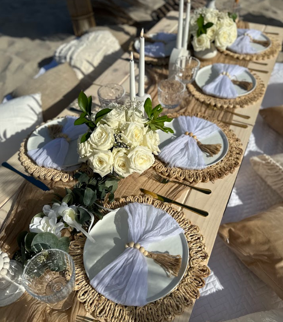 Beach picnic table setting with white flowers, candles, and woven placemats.