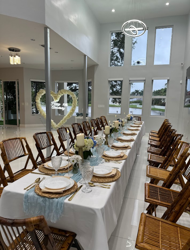 Long table set for a formal event, with decor, chairs, and large windows.