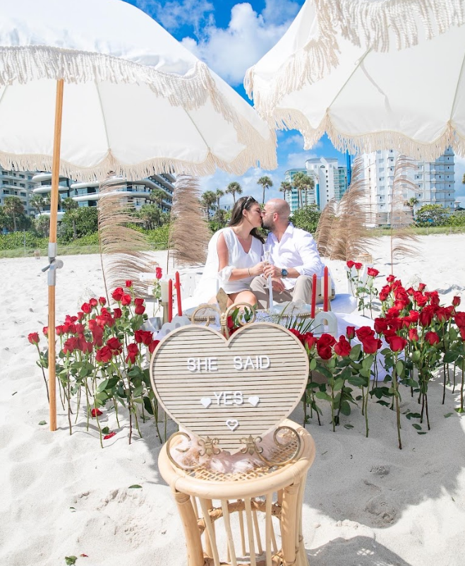 Couple kissing under beach umbrellas, surrounded by roses;