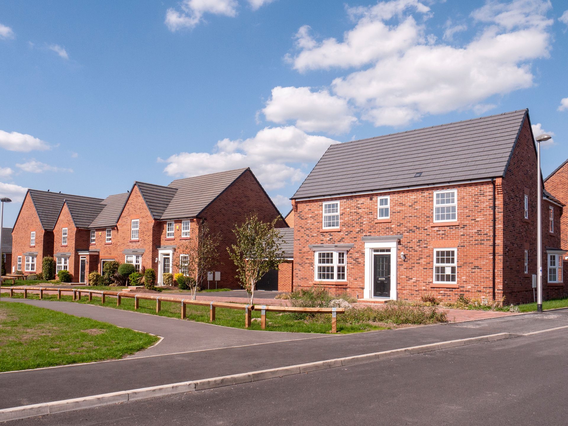 Row of red brick houses on a sunny day with a pathway and small grassy area.