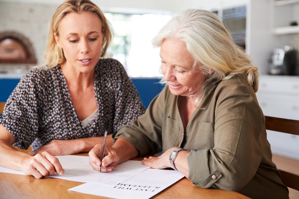 Two women are sitting at a table writing on a piece of paper.