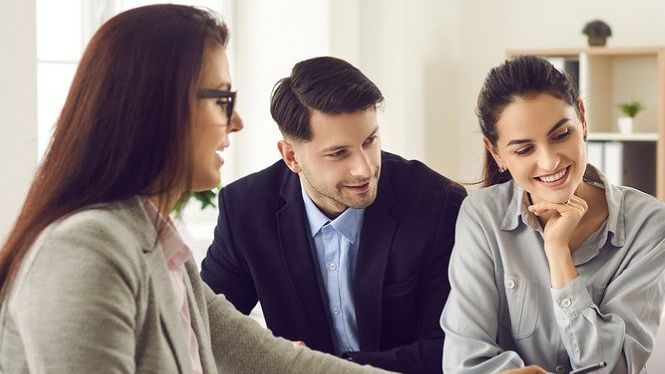 A man and a woman are sitting at a table talking to a woman.