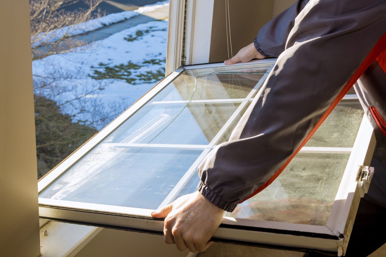 Person carrying a white-framed window through an open window, with snowy outdoors visible.